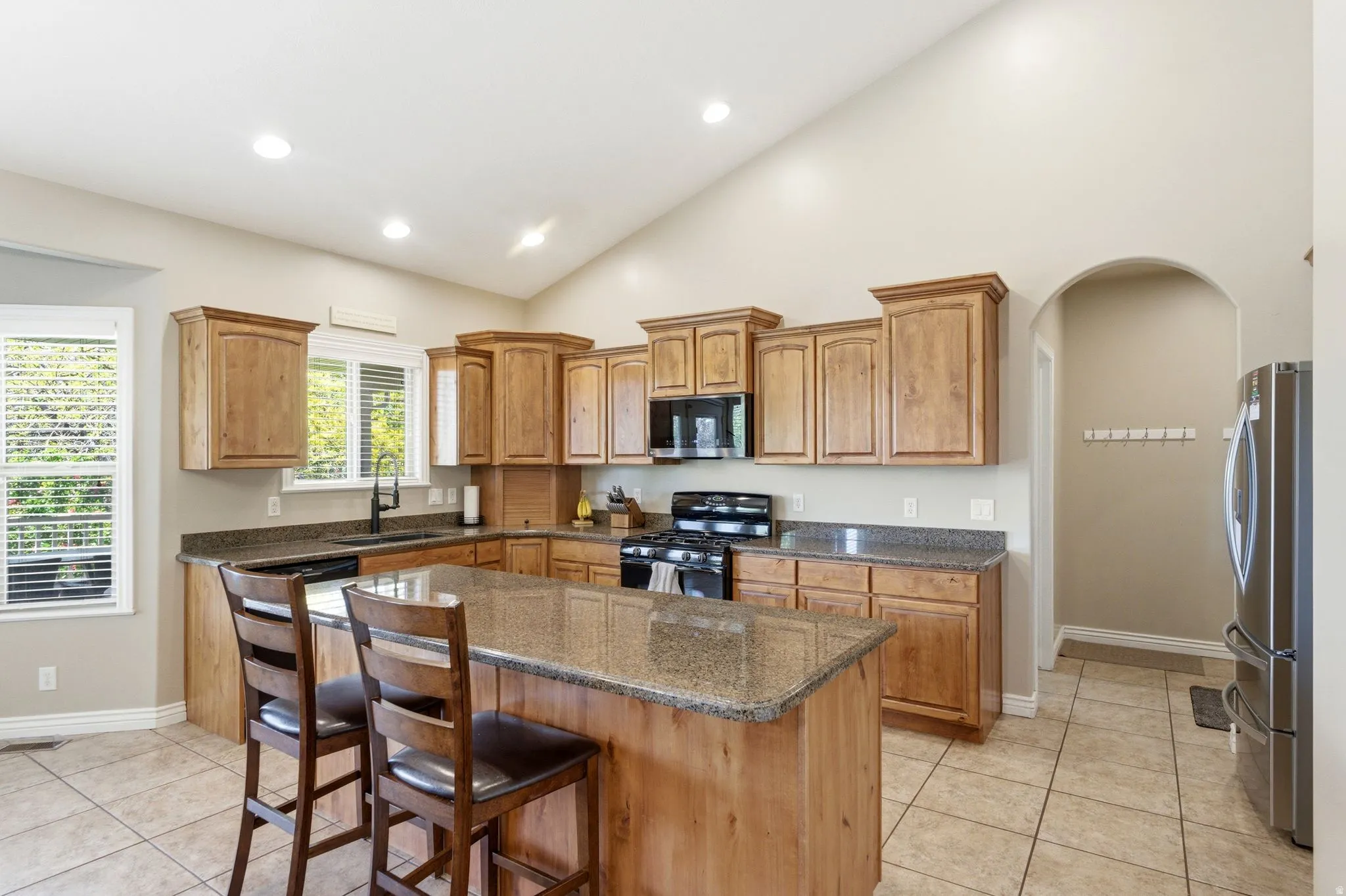 Kitchen featuring a large island with seating, ample wood cabinetry, dark countertops, and tile flooring