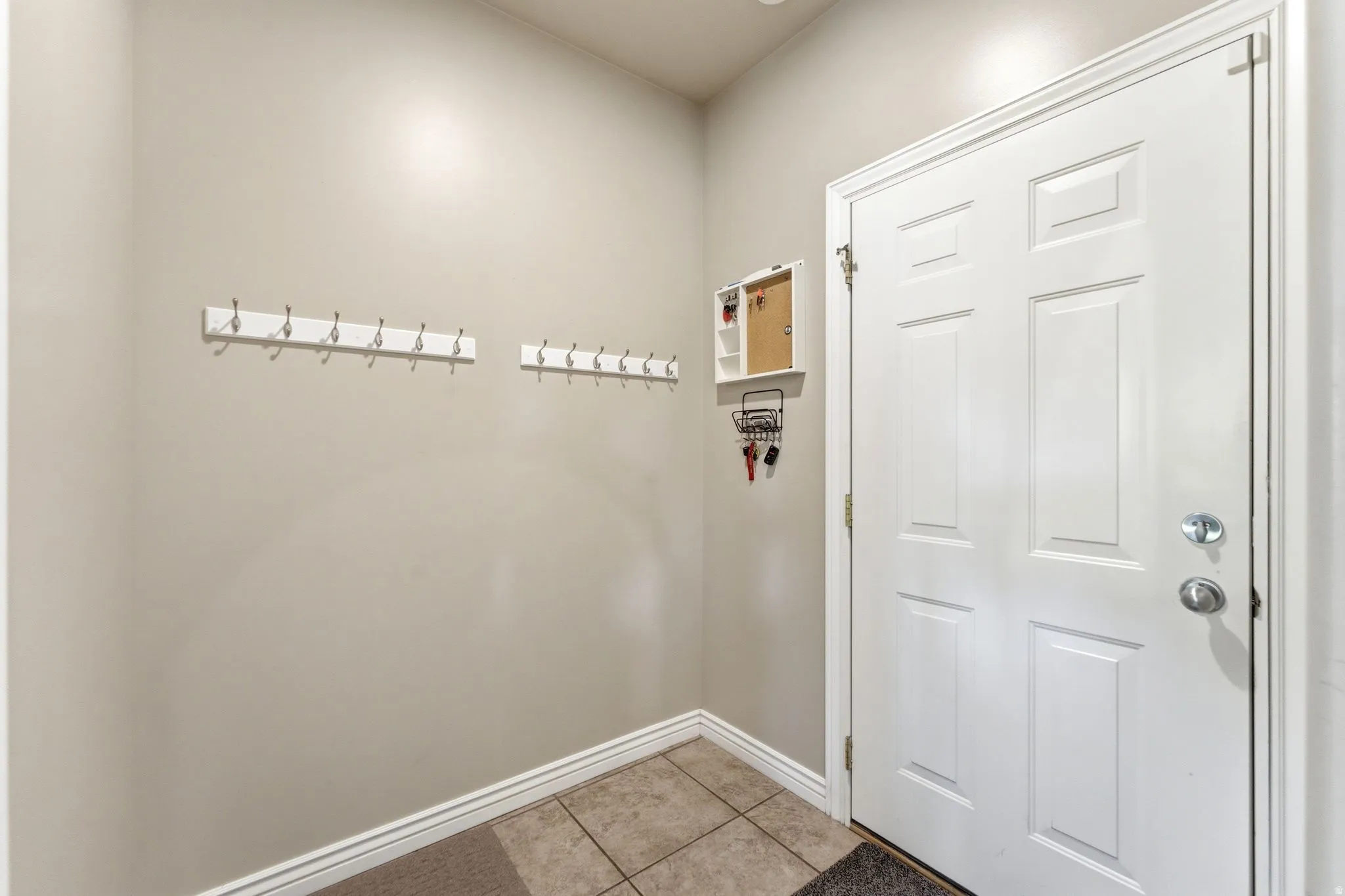 Entryway featuring a white paneled door, ceramic tile flooring, and two wall-mounted coat racks