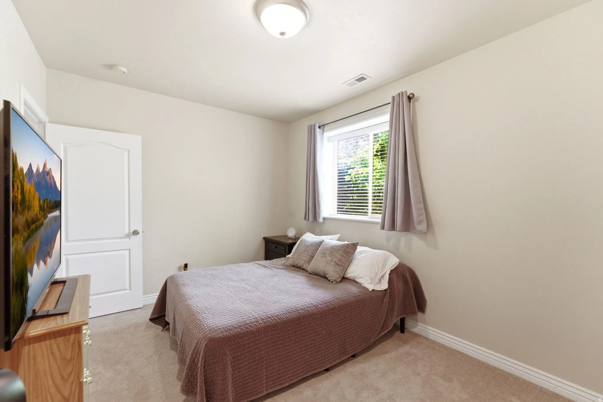 Neutral-toned room featuring a single window with blinds, carpeted flooring, and a flush mount ceiling light fixture