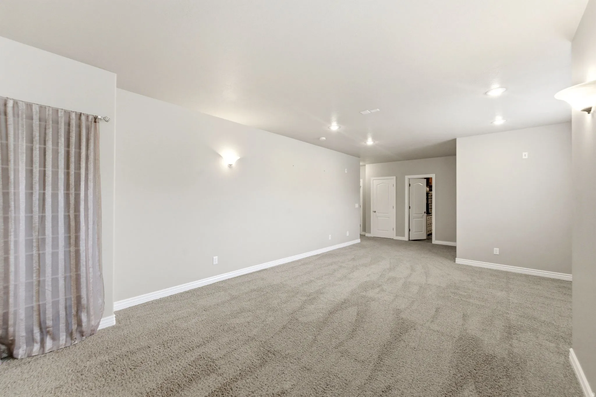Spacious room featuring neutral carpet, light gray wall paint, white trim, recessed ceiling lighting, and wall sconces