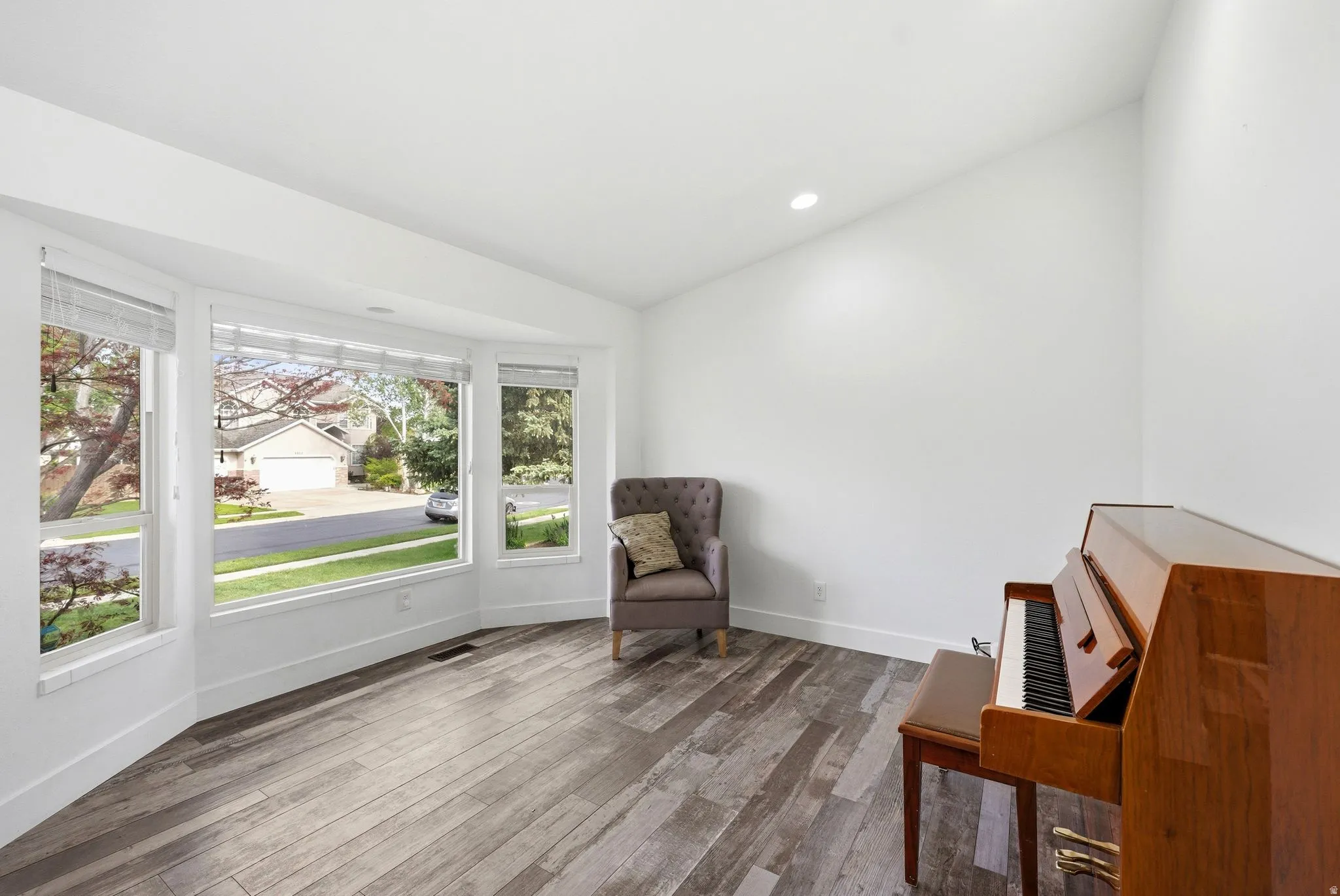 Bay window with multiple panes, wood-finish flooring, white walls, recessed lighting, and a vaulted ceiling