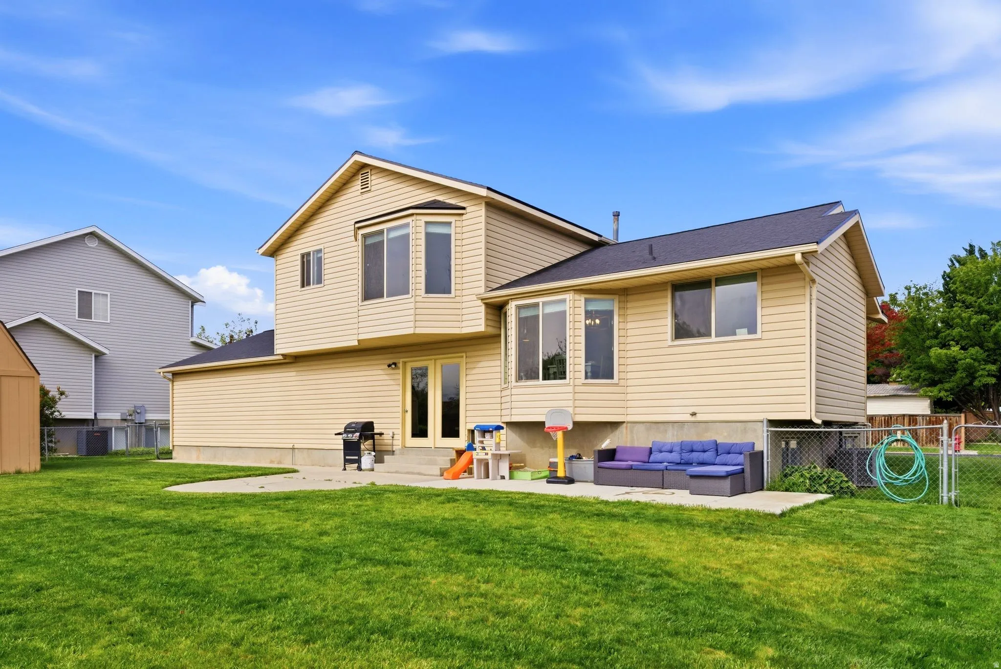Expansive backyard featuring a manicured lawn, a concrete patio, and a chain-link fence