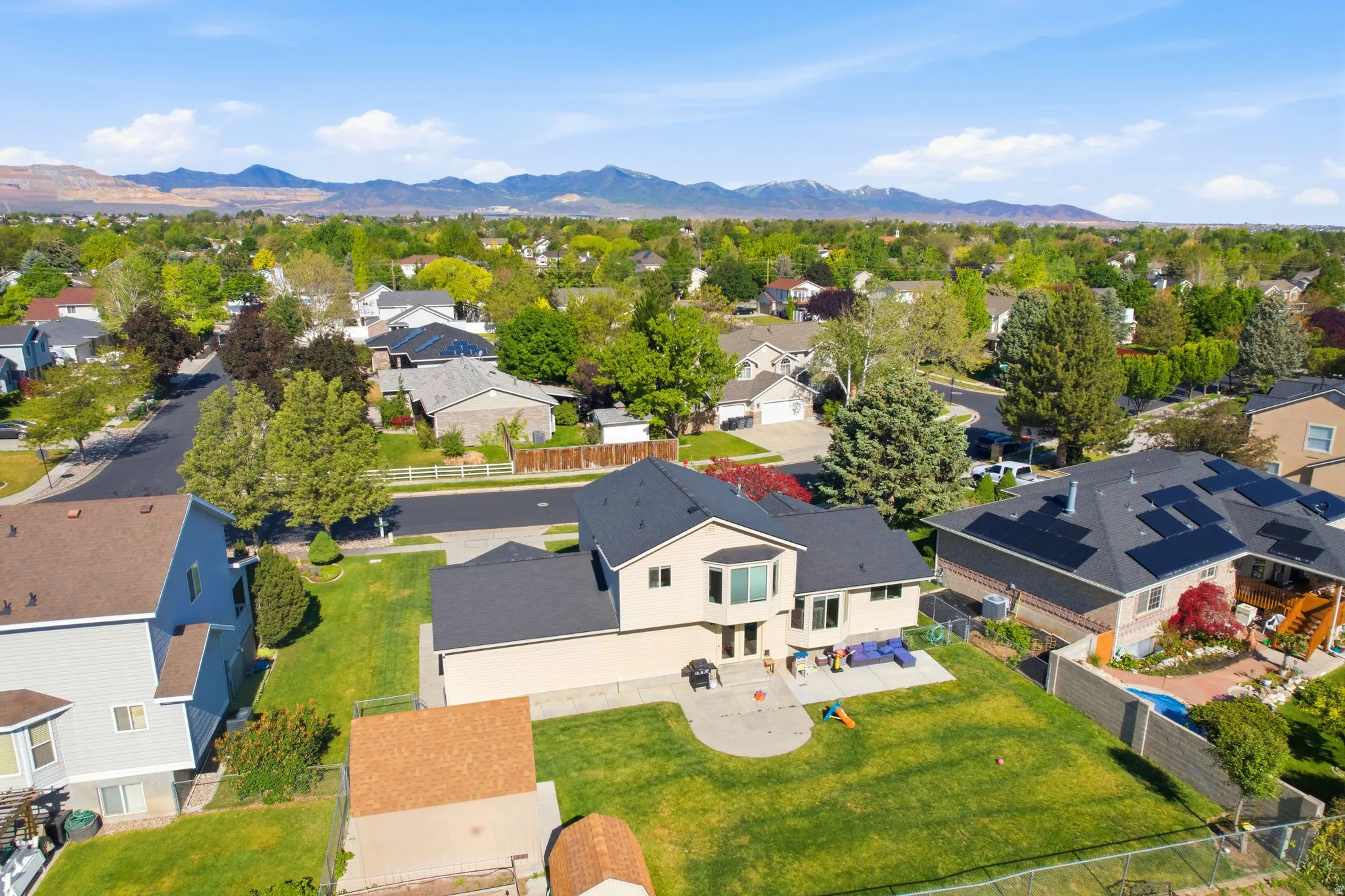 Expansive green lawn with a large patio area, mature trees, and mountain scenery in the distance