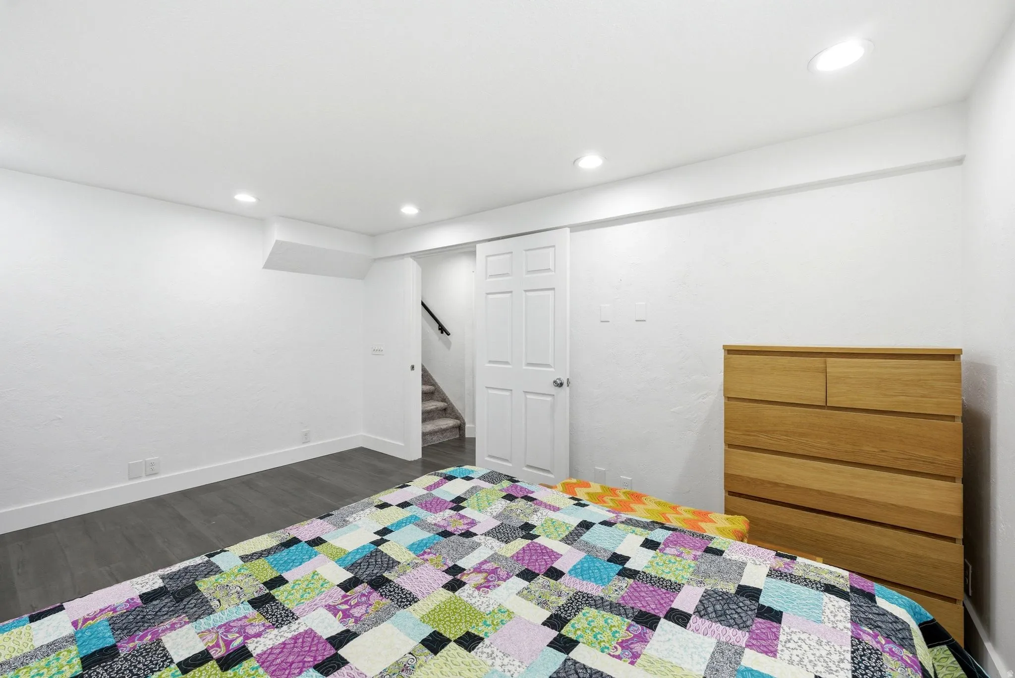Recessed lighting illuminates this room, featuring wood-finish flooring and white baseboards