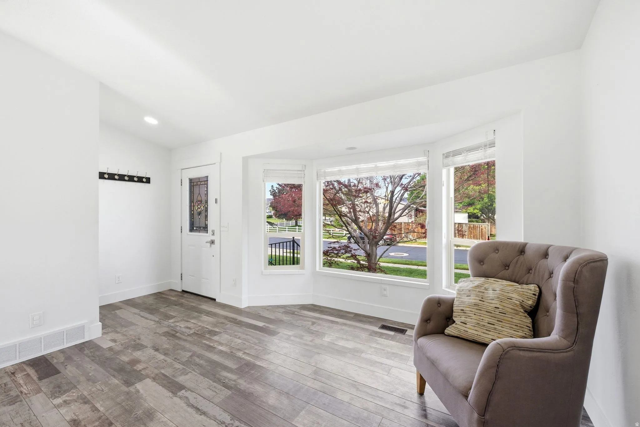 Inviting interior space featuring wood-finish flooring, a white paneled entry door with decorative glass, and a prominent bay window