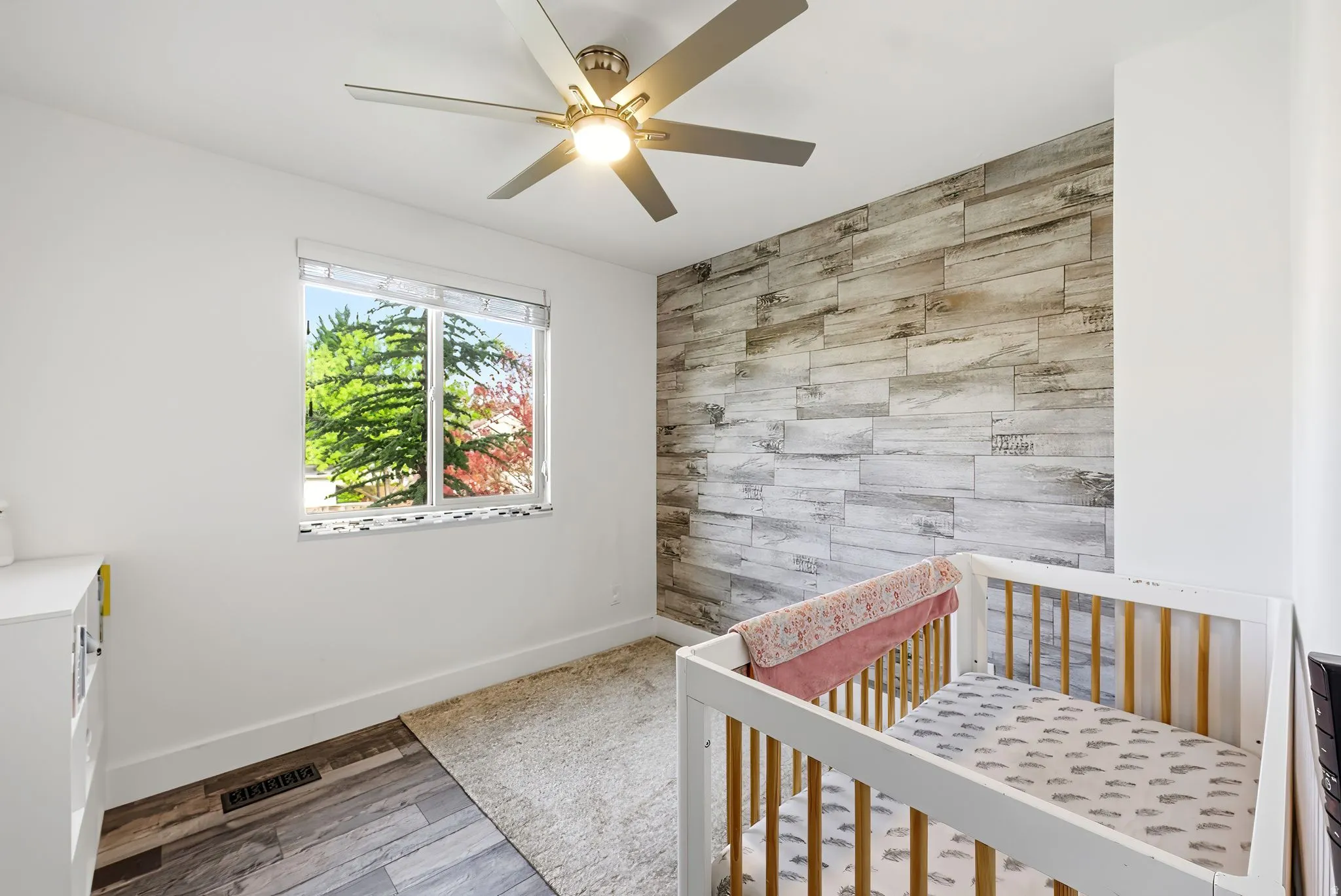 Bedroom featuring a decorative wood-panel accent wall, wood-finish flooring, and a ceiling fan with integrated lighting