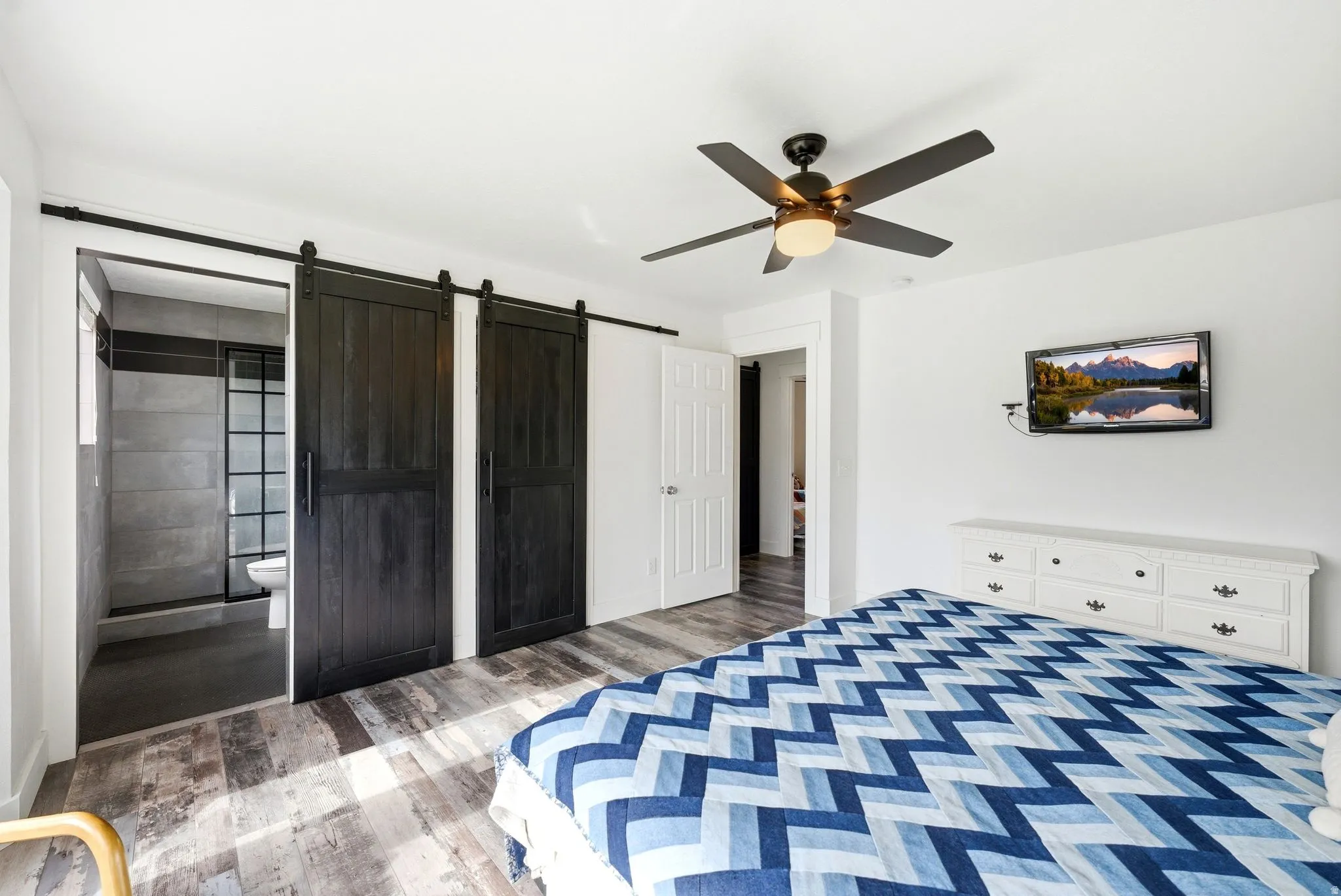 Spacious room featuring wood-finish flooring, a ceiling fan with integrated lighting, and white walls