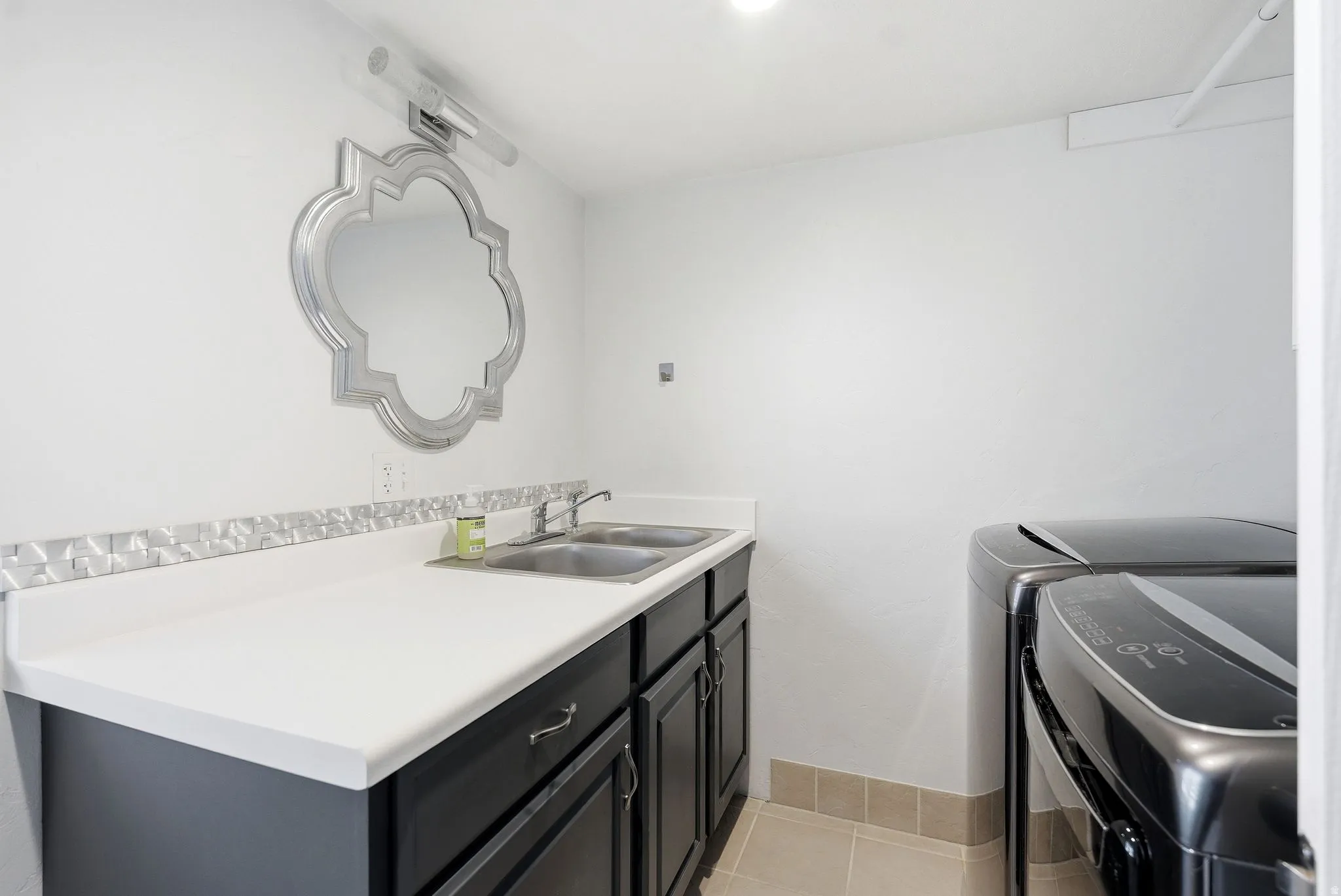Laundry area featuring a built-in countertop with dual stainless steel sinks, dark wood-finish cabinetry with silver hardware, and a decorative silver mirror