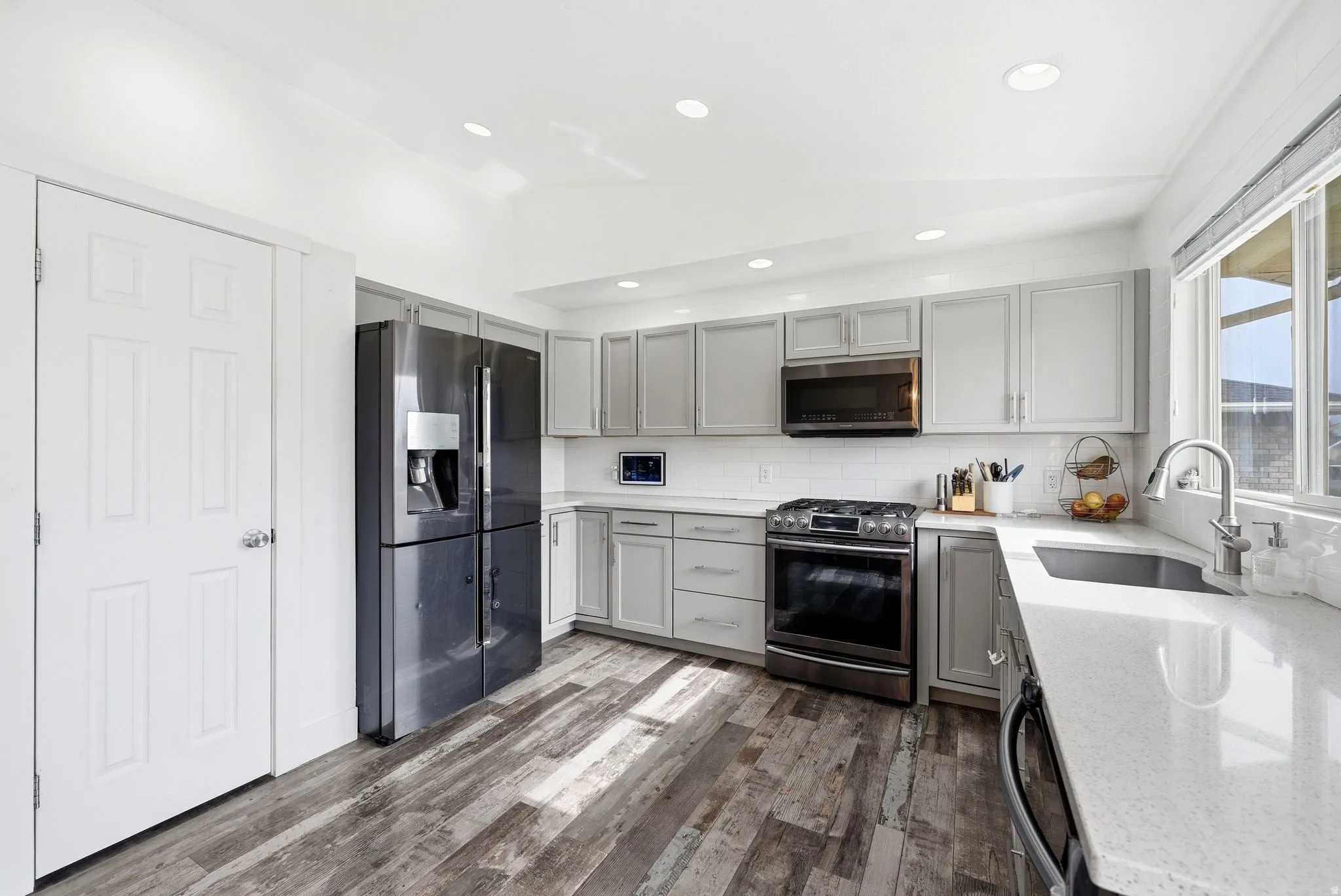 Kitchen featuring light gray cabinetry, white countertops, wood-finish flooring, stainless steel appliances, and a white subway tile backsplash