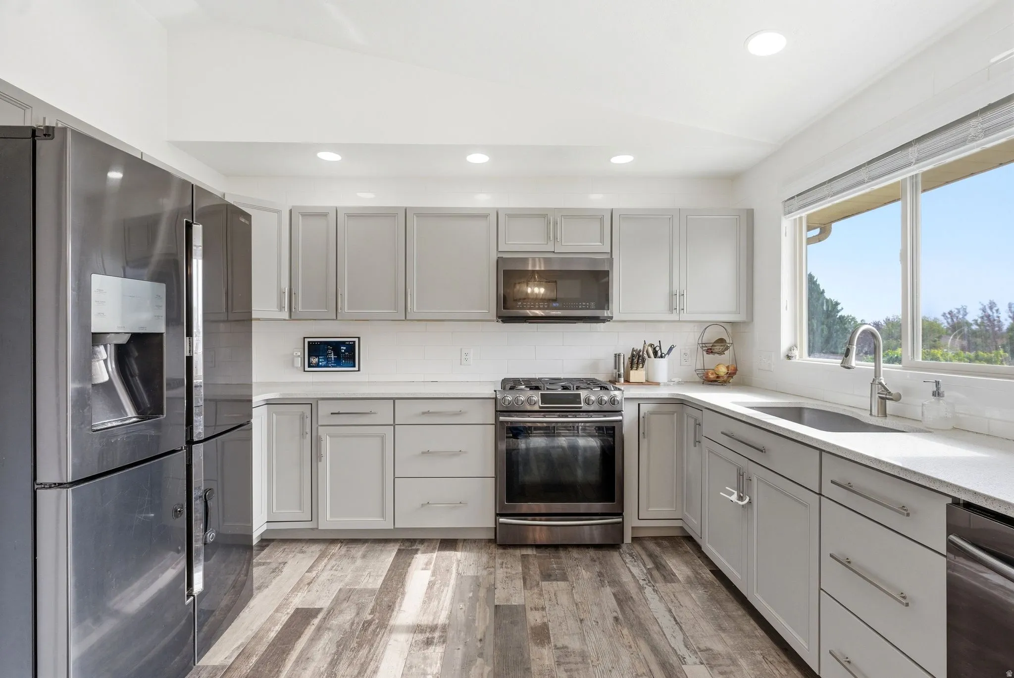 Modern kitchen featuring wood-finish flooring, white shaker cabinetry, white subway tile backsplash, and light-colored countertops