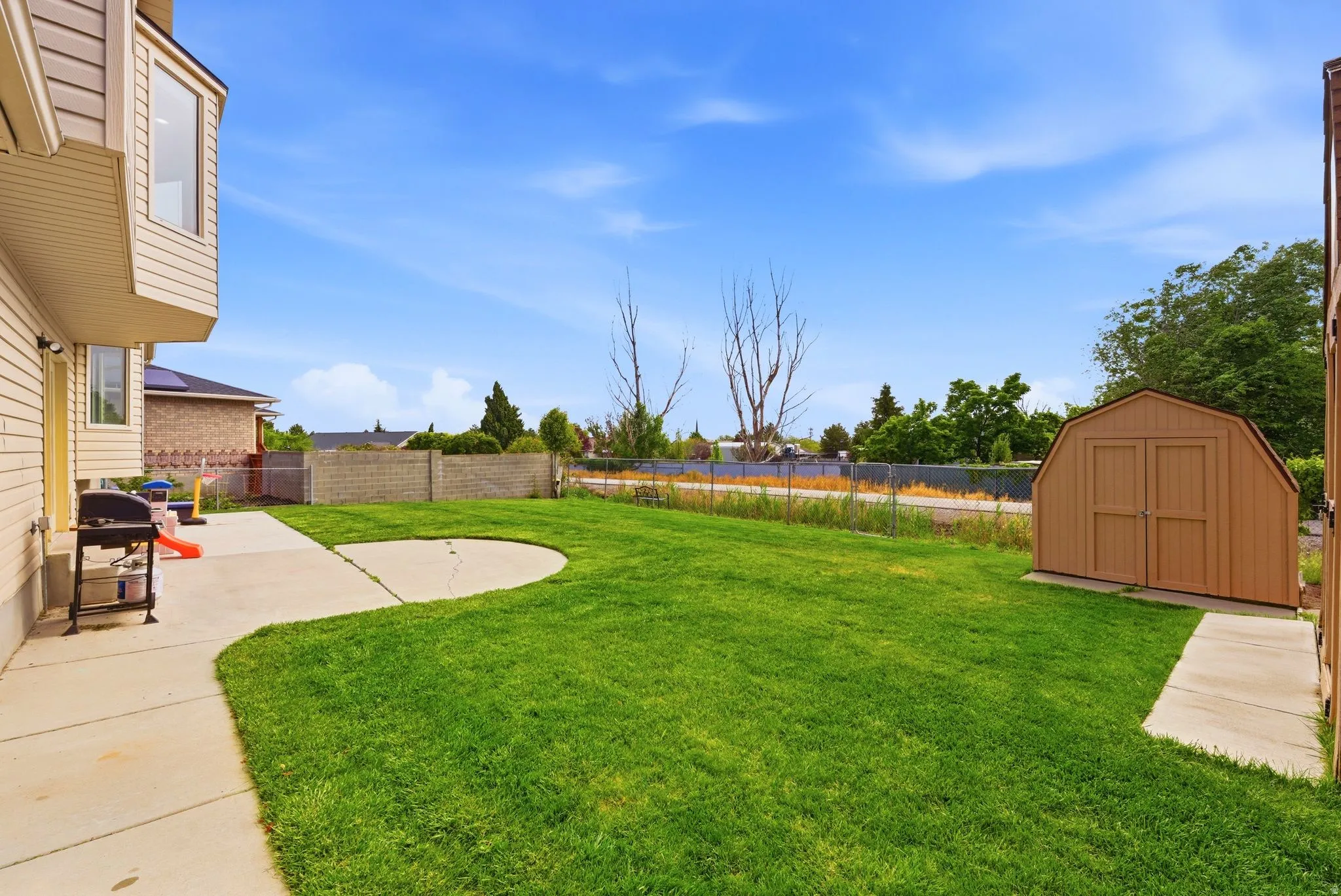 Expansive backyard featuring a large grass lawn, a curved concrete patio, and a dedicated storage shed