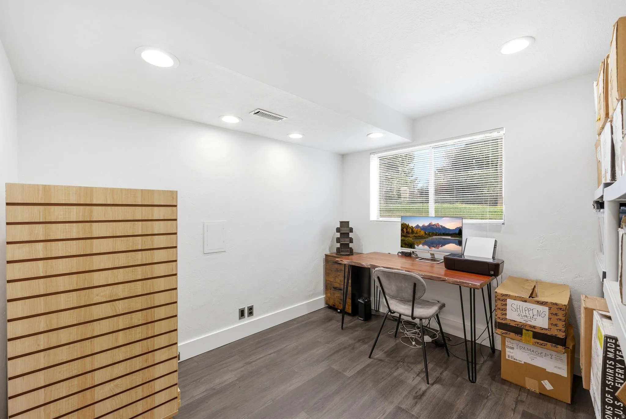 Recessed lighting illuminates this room featuring wood-finish flooring, white baseboards, and a window with horizontal blinds