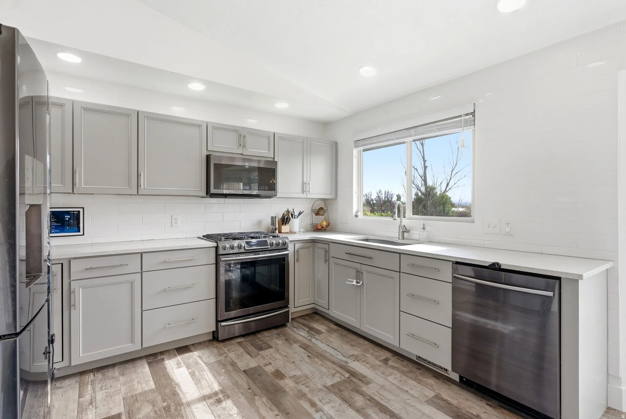 Modern kitchen featuring light gray cabinetry, stainless steel appliances, white subway tile backsplash, and wood-finish flooring