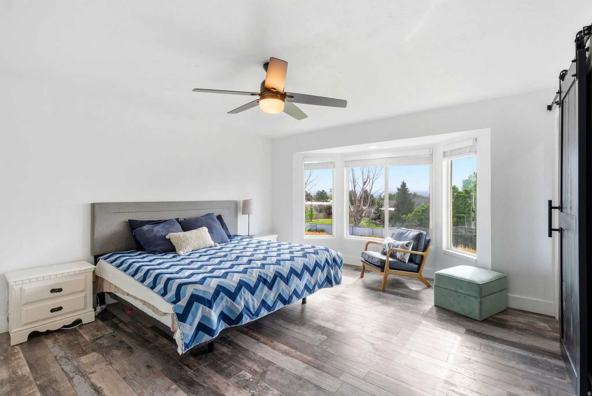 Spacious room featuring wood-finish flooring, a contemporary ceiling fan, and a large bay window