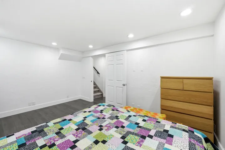 Recessed lighting illuminates this room, featuring wood-finish flooring and white baseboards