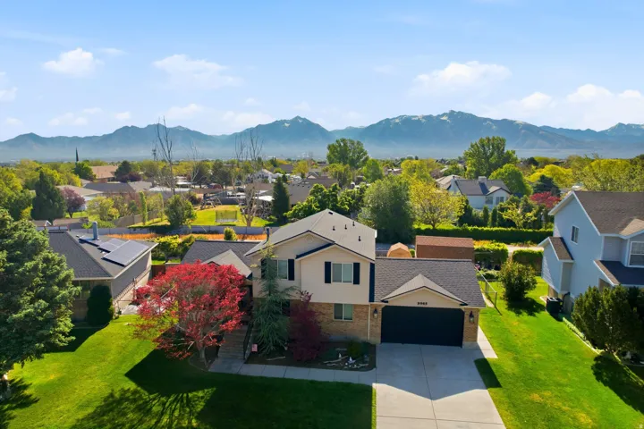 Two-story residence featuring a two-car garage, manicured front lawn, and mature trees, set against a distant mountain backdrop