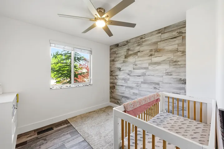 Bedroom featuring a decorative wood-panel accent wall, wood-finish flooring, and a ceiling fan with integrated lighting