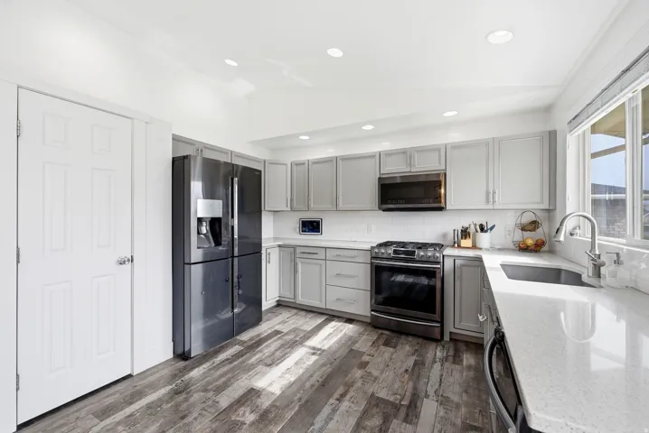 Kitchen featuring light gray cabinetry, white countertops, wood-finish flooring, stainless steel appliances, and a white subway tile backsplash