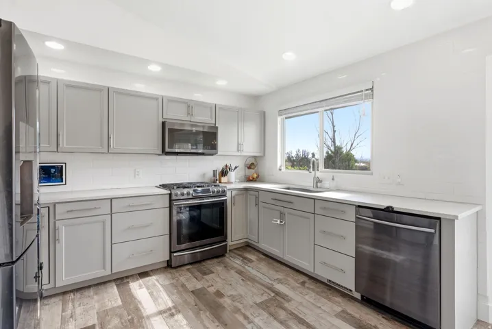 Modern kitchen featuring light gray cabinetry, stainless steel appliances, white subway tile backsplash, and wood-finish flooring