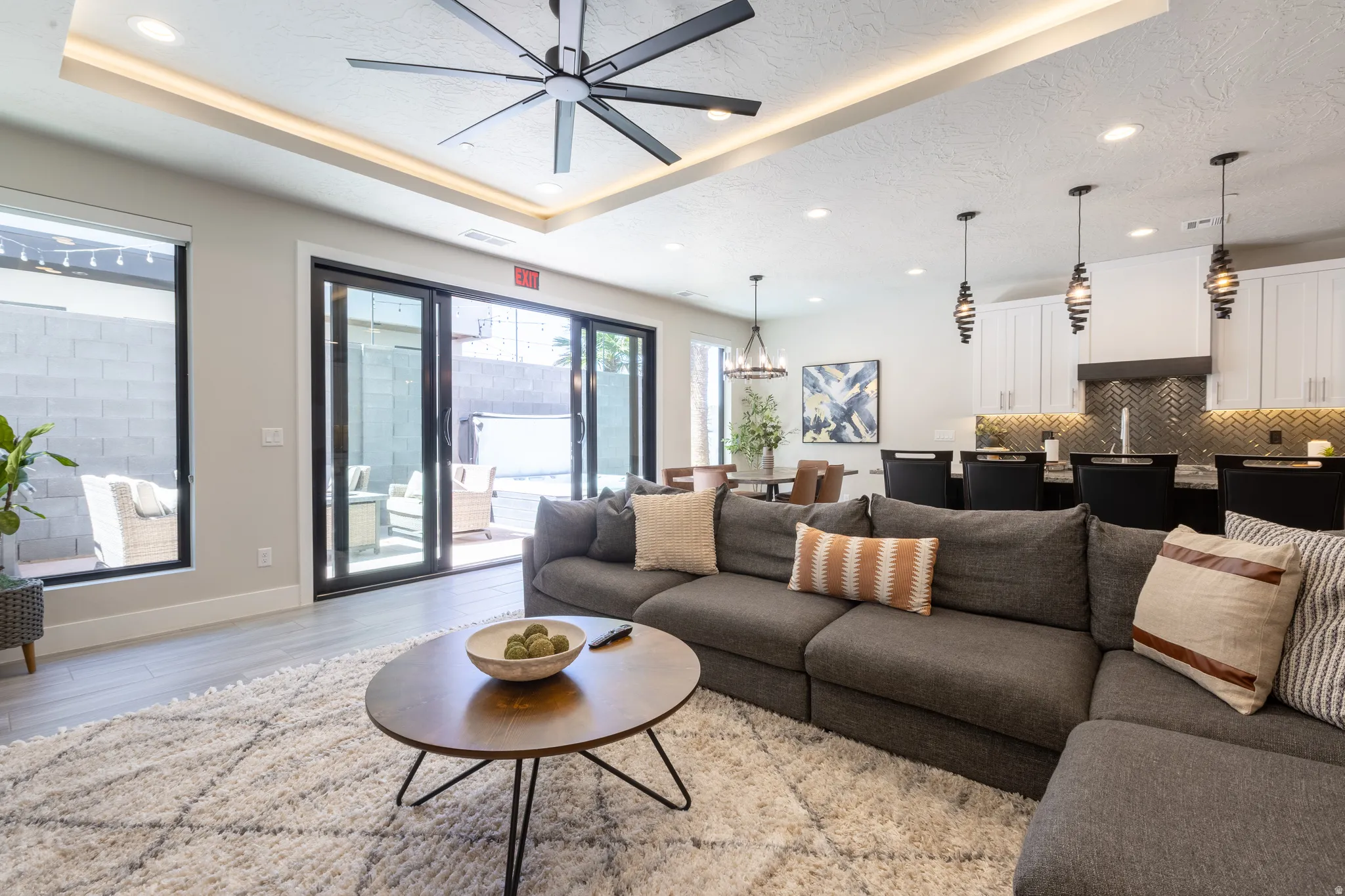 Open-concept living area with large sliding glass doors, wood-finish flooring, a tray ceiling with recessed lighting, and a modern ceiling fan