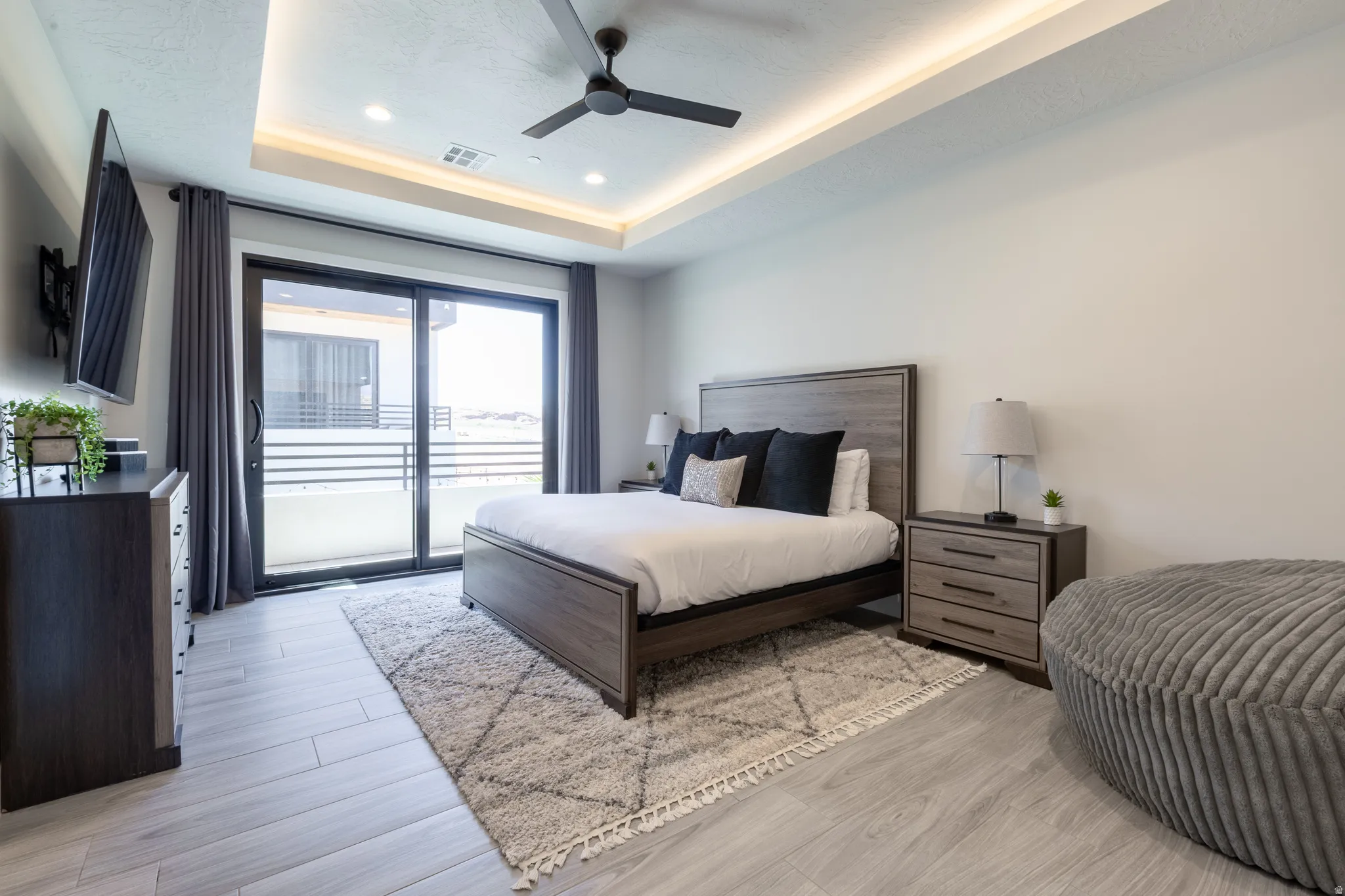 Bedroom featuring a sliding glass door to a private balcony, tray ceiling with recessed lighting and a ceiling fan, and wood-finish flooring