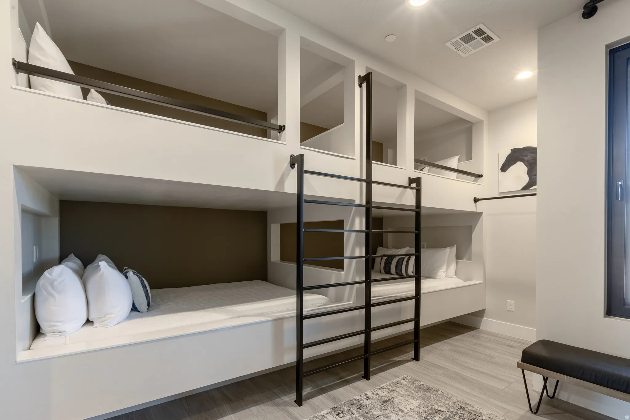 Built-in bunk beds with integrated storage niches, a black metal ladder, and light wood-finish flooring