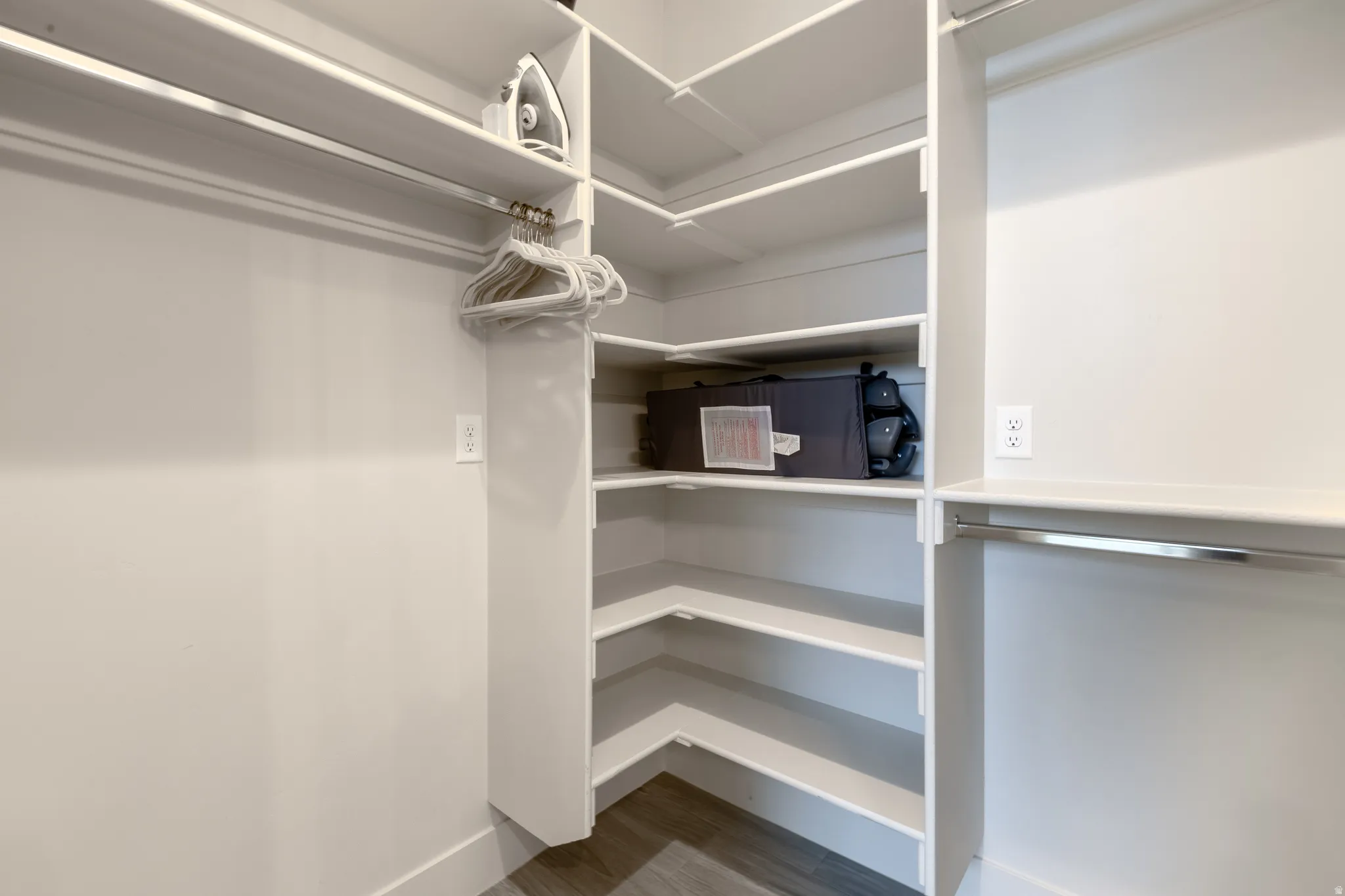 Walk-in closet featuring extensive built-in shelving, multiple hanging rods, corner shelves, electrical outlets, and wood-finish flooring