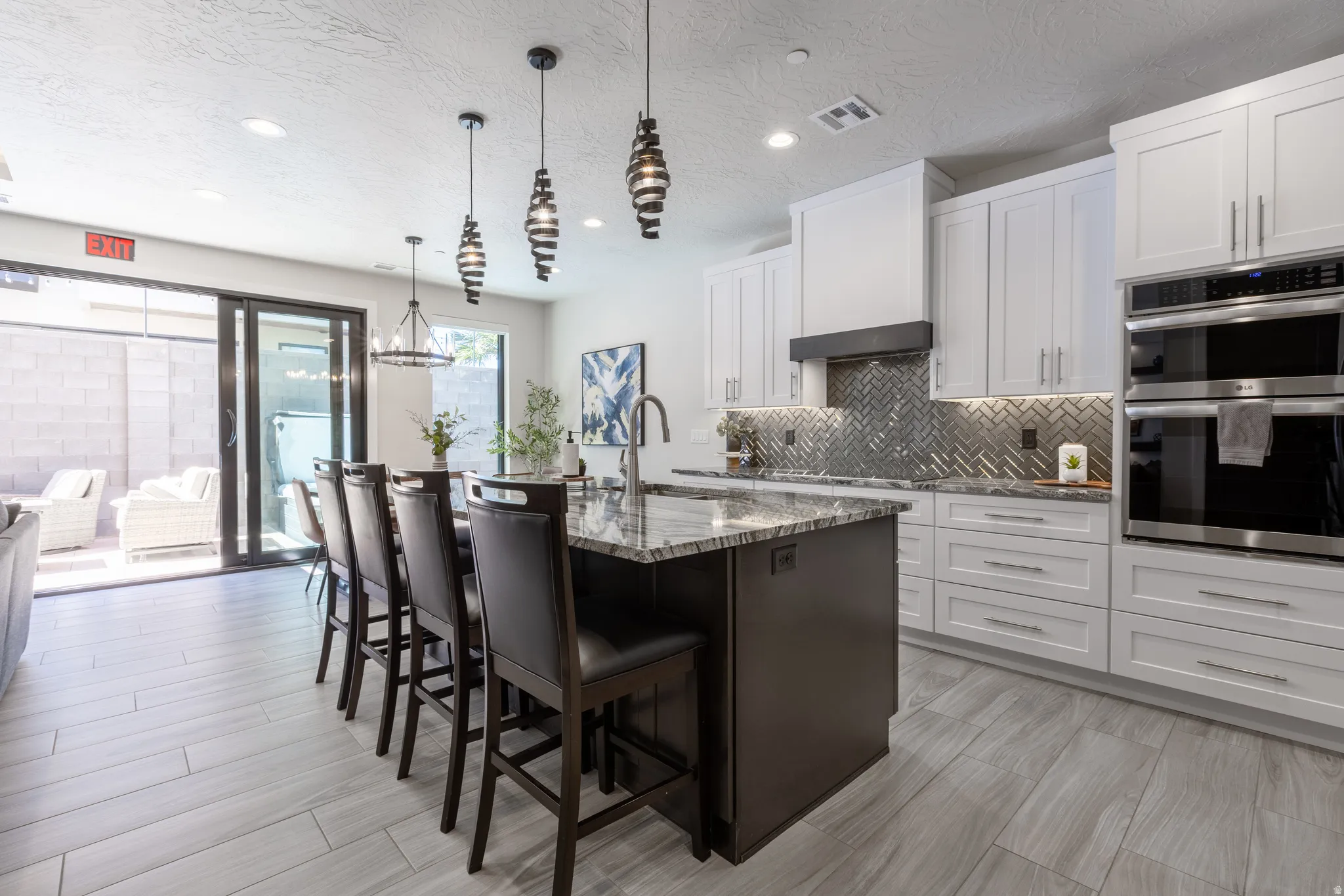 Modern kitchen featuring a large island with seating, white shaker cabinetry, stainless steel double ovens, and a herringbone tile backsplash