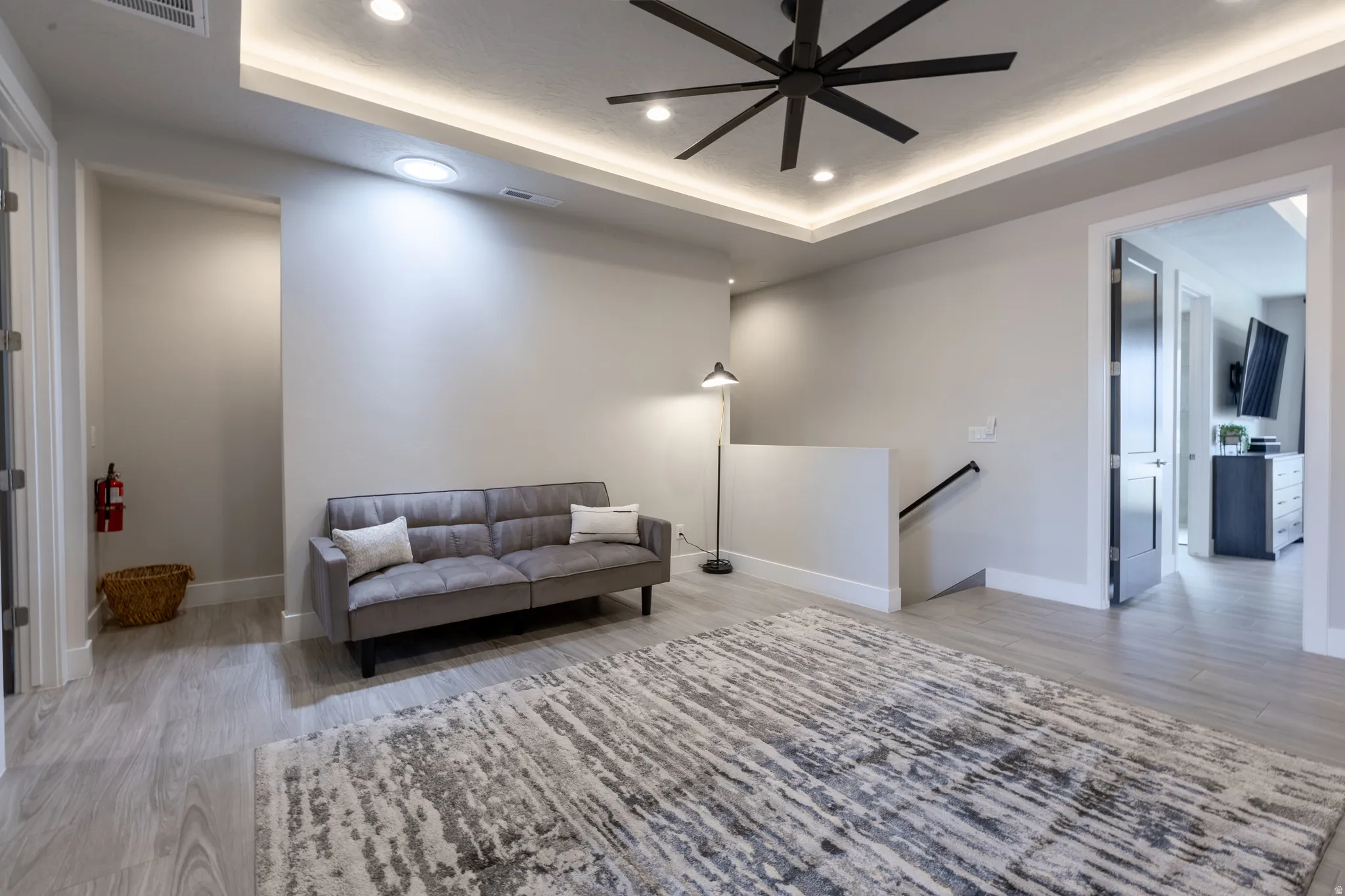 Open concept living area featuring recessed lighting, a ceiling fan, tray ceiling, light wood-finish flooring, and crisp white baseboards