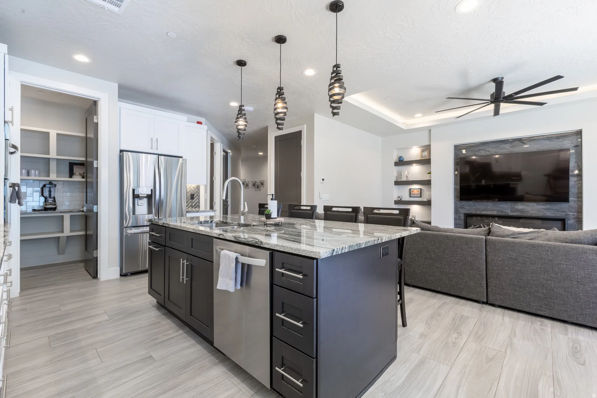 Open-concept kitchen featuring a large island with integrated sink, stainless steel appliances, and a walk-in pantry with shelving