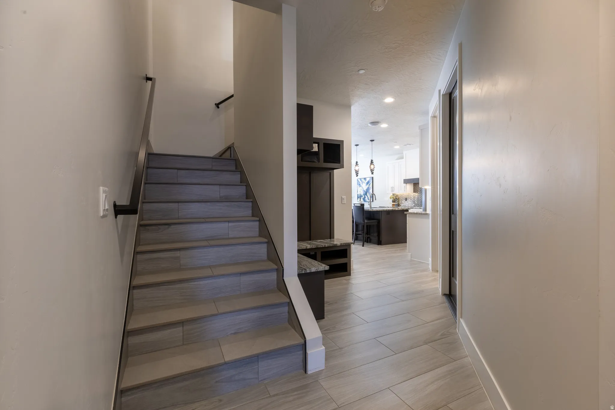 Entryway featuring wood-finish flooring extending into the hallway, a built-in dark wood accent piece with open shelving, and a contemporary staircase with dark wood-finish handrails