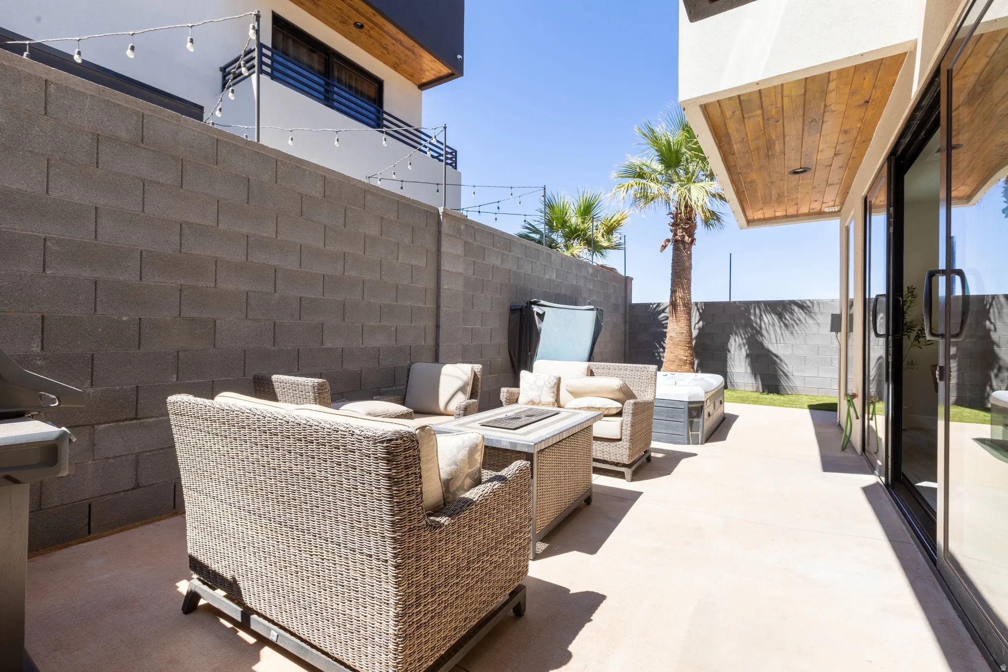 Expansive outdoor patio with concrete flooring, block privacy wall, and mature palm trees