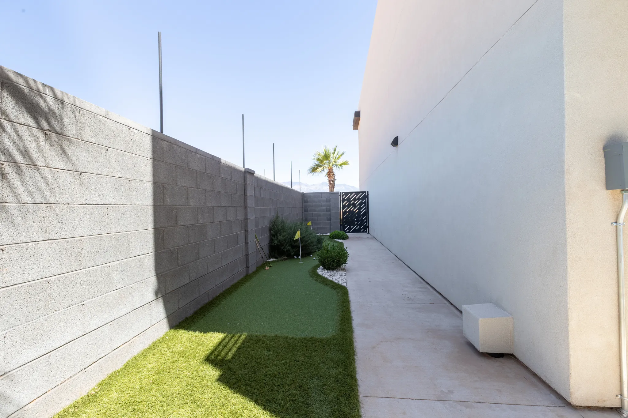 Side yard featuring a putting green, artificial turf, concrete pathway, decorative gravel, and a block wall perimeter