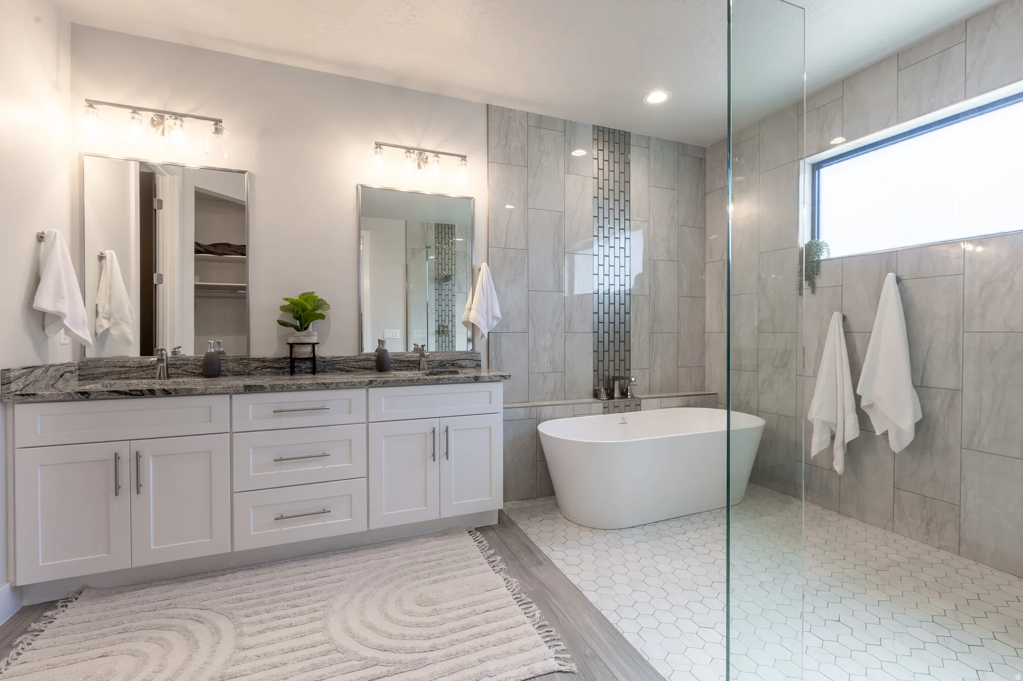 Bathroom featuring a double vanity with stone countertops, a freestanding soaking tub, and a glass-enclosed shower