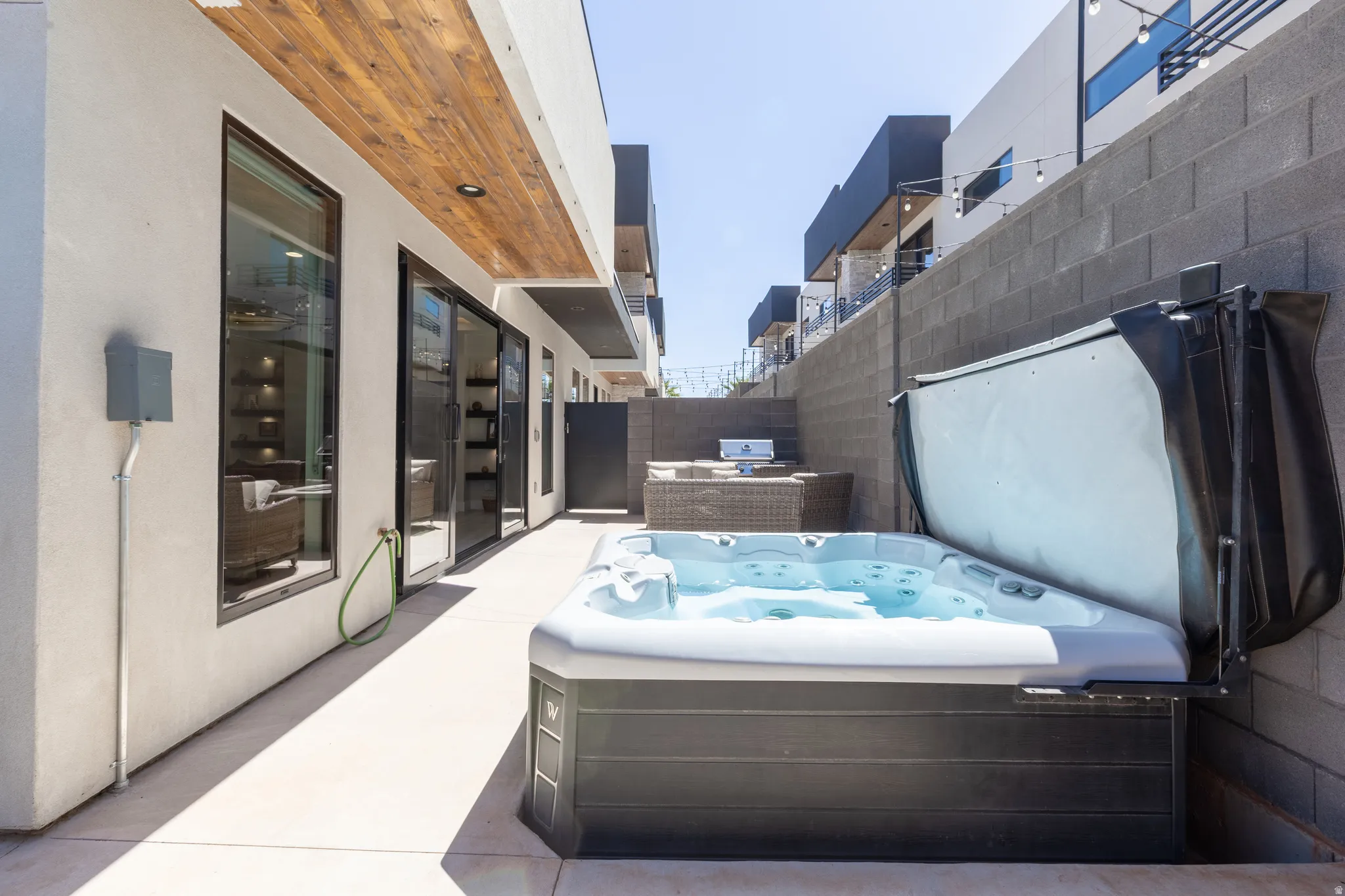 Outdoor patio with a built-in spa, concrete flooring, sliding glass doors, large picture windows, and a wood-finish ceiling accent