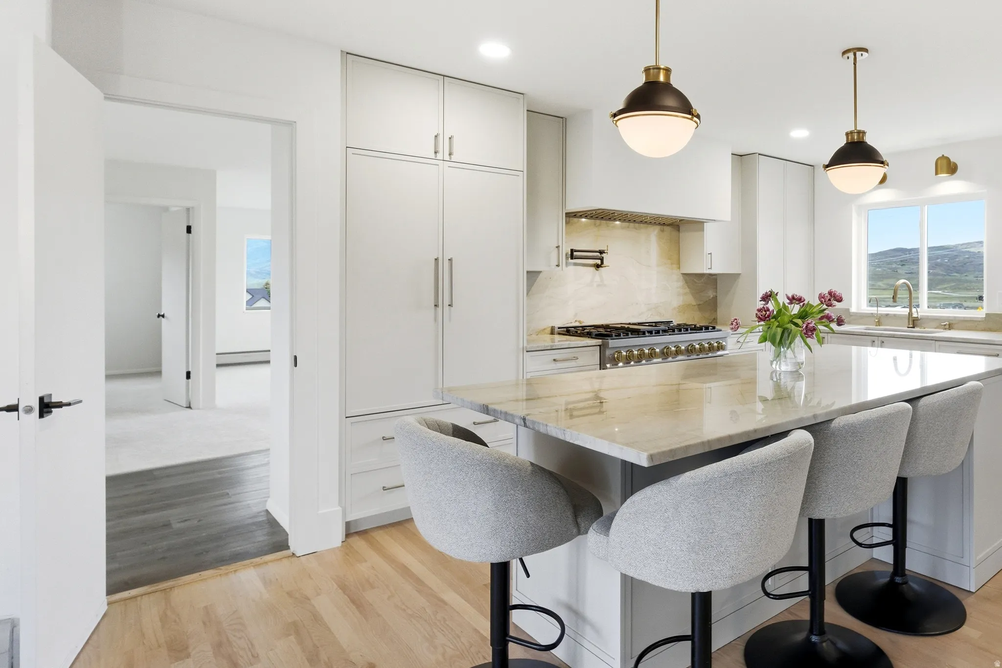 Modern kitchen featuring a large island with a stone countertop, built-in range with pot filler, integrated refrigerator, and light wood-finish flooring
