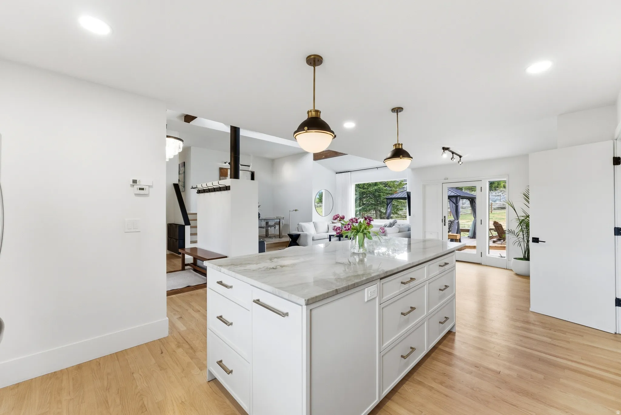 Kitchen island with stone countertop, brass pendant lighting, light wood-finish flooring, white cabinetry, and recessed lighting
