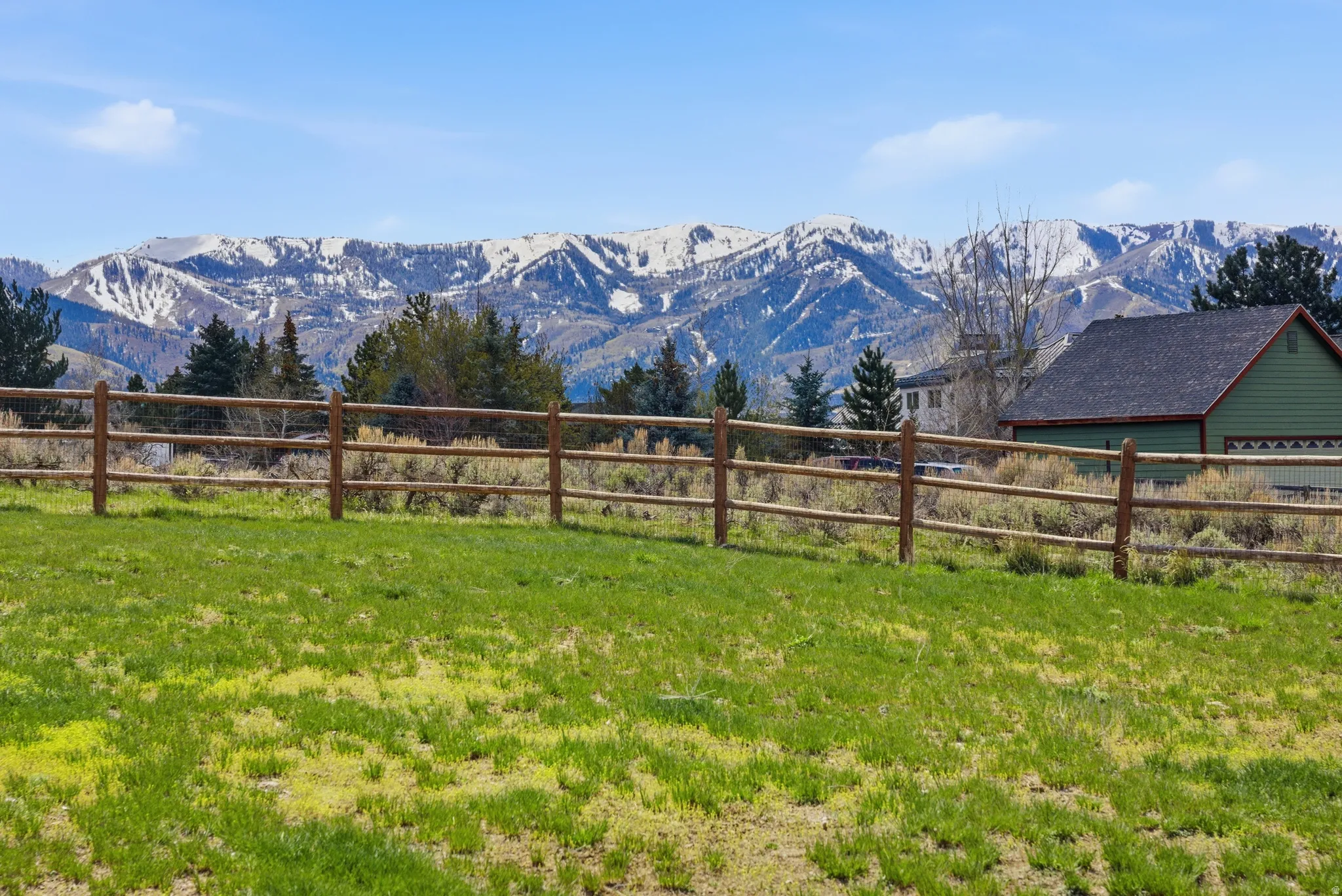 Expansive green space featuring a rustic split-rail fence, backed by a range of snow-capped mountains