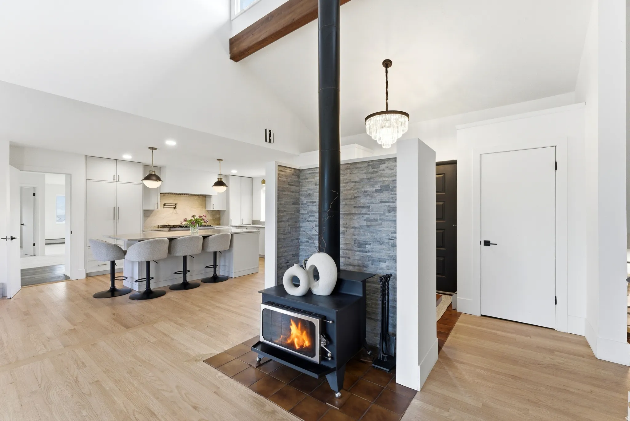 Vaulted ceilings with exposed wood beam, wood-finish flooring, and a free-standing stove with stone veneer surround