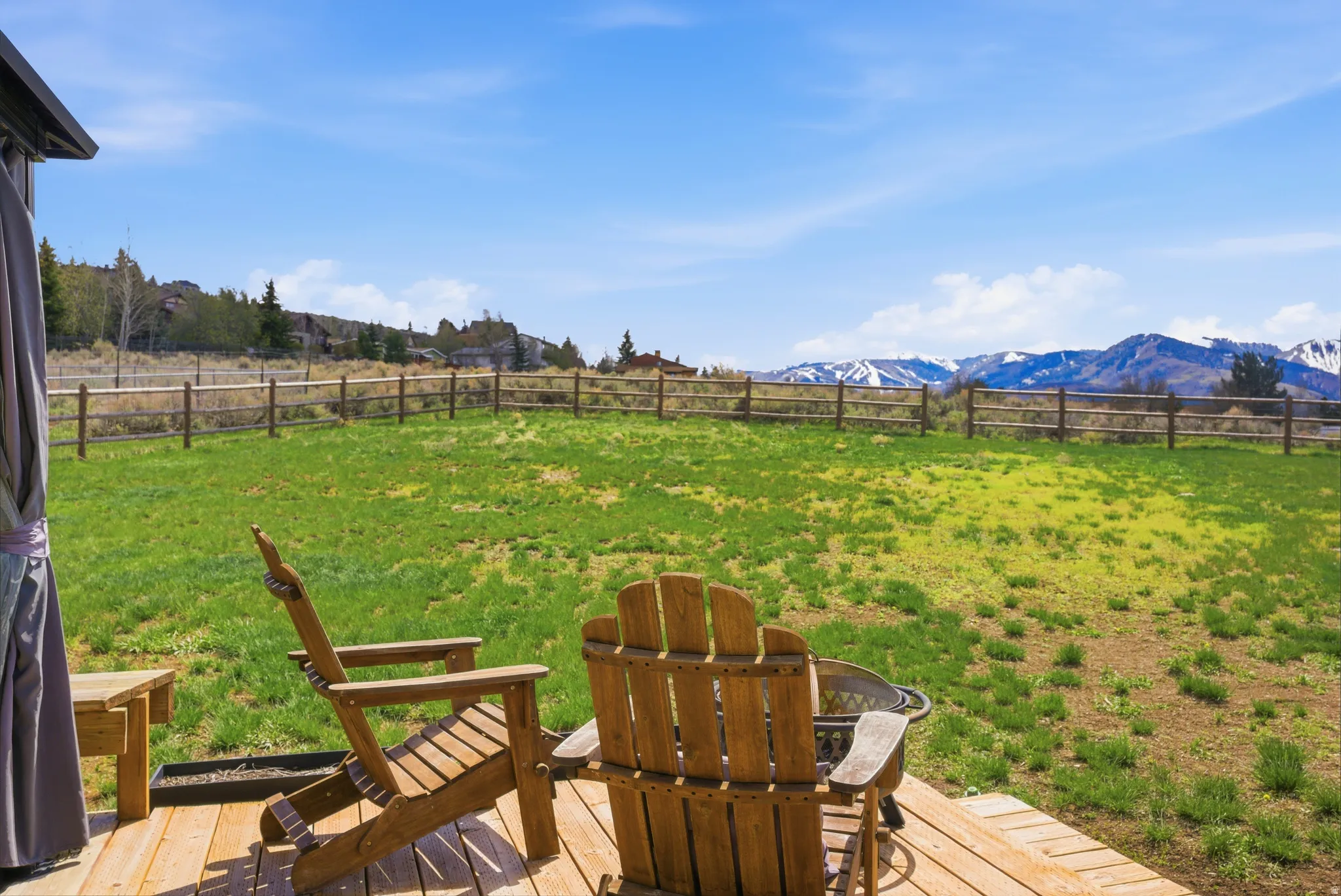 Expansive backyard featuring a lush lawn, split-rail fencing, and distant mountain scenery