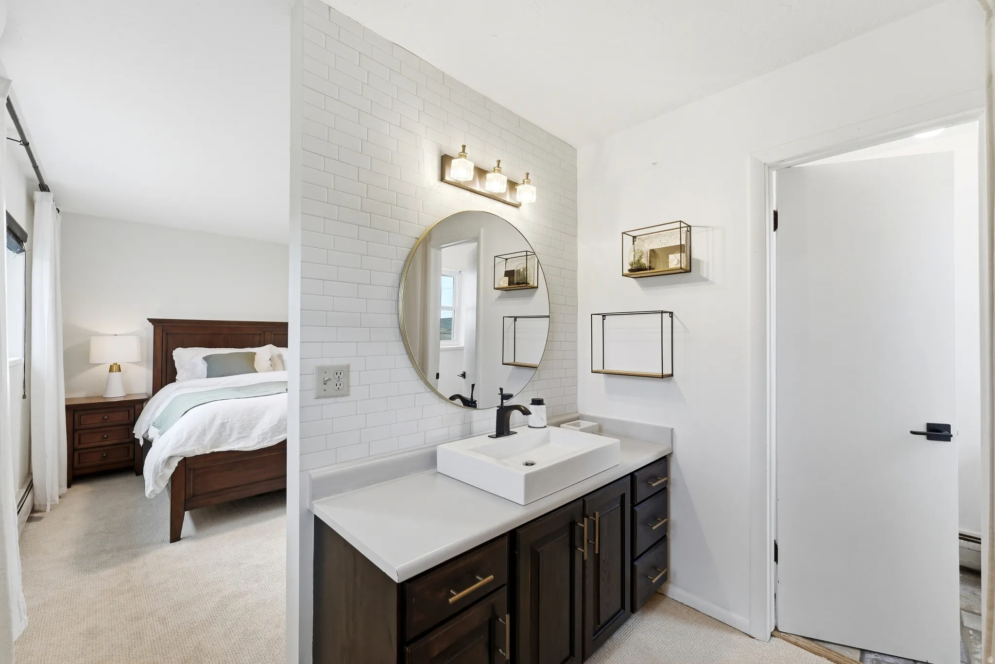 Bathroom vanity featuring a vessel sink, dark wood cabinetry with gold-toned hardware, and a round mirror