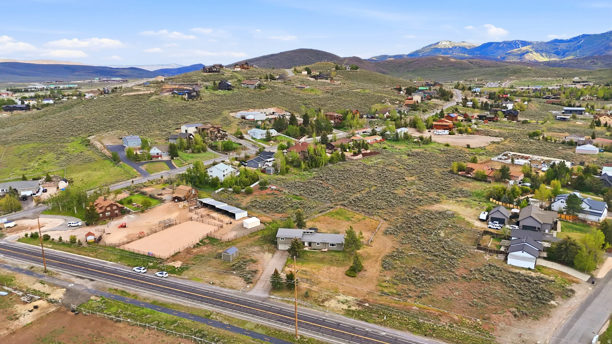 Expansive land parcel featuring an established residential structure, unpaved driveway, and surrounding natural topography with distant mountain ranges