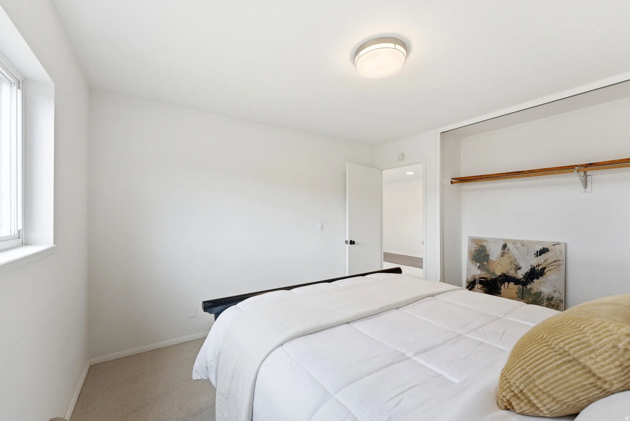 Carpeted room featuring a window with vertical blinds, a flush-mount ceiling light, and an open closet with a wood-finish hanging rod