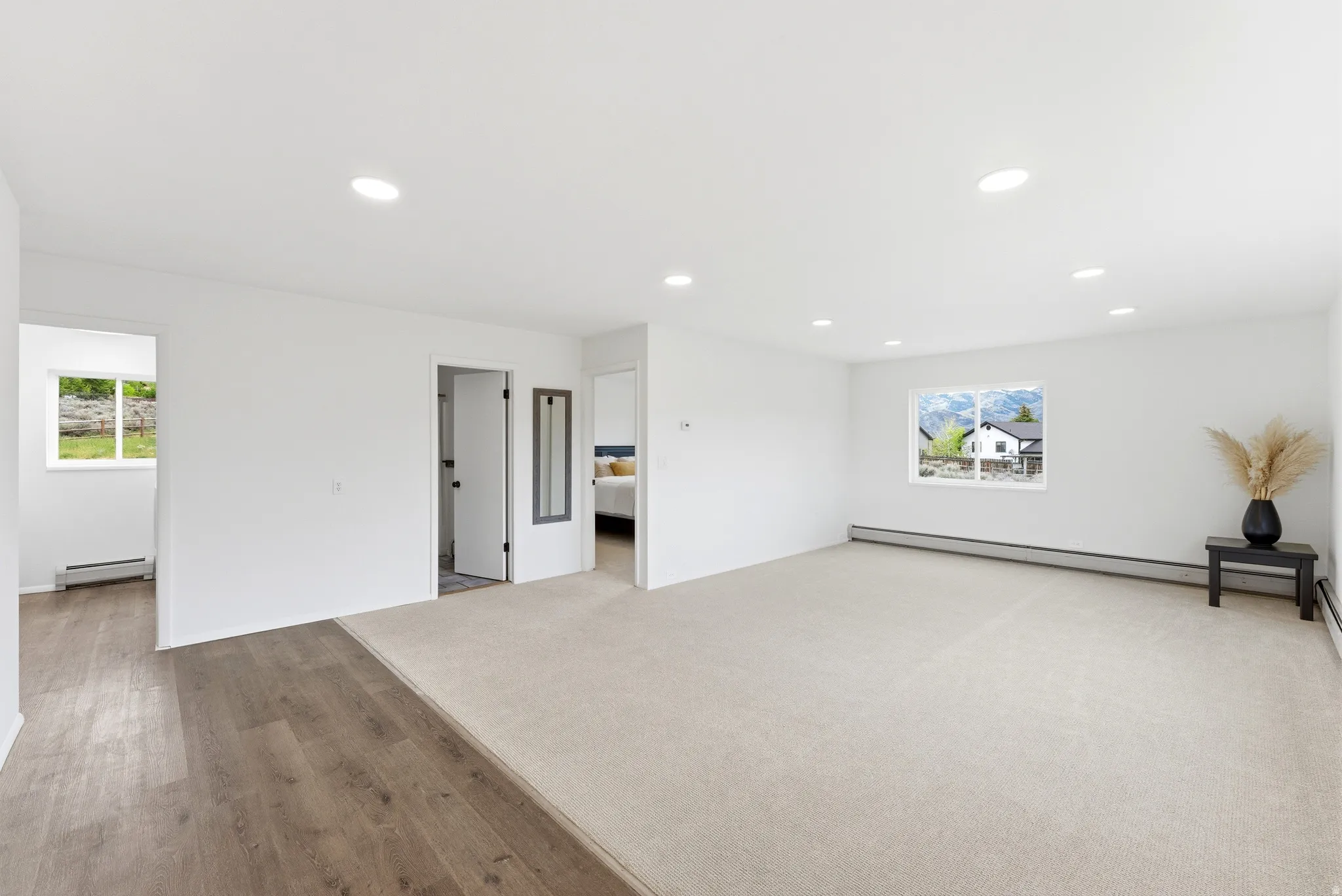Bright interior space featuring recessed lighting, a large window, light-toned carpeting, wood-finish flooring, and white painted walls