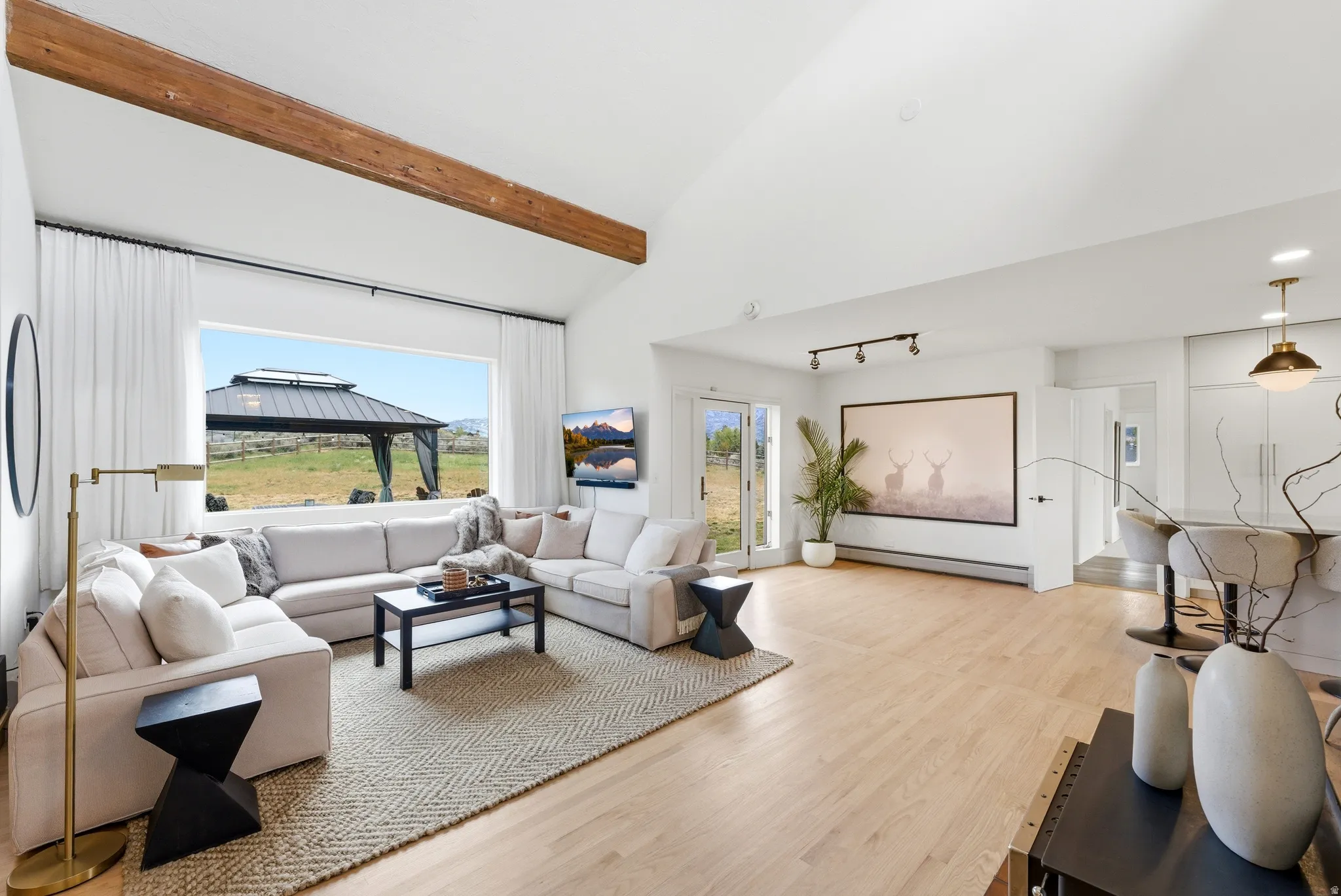 Spacious living area featuring a vaulted ceiling with exposed wood beams, a large picture window, light wood-finish flooring, and recessed lighting