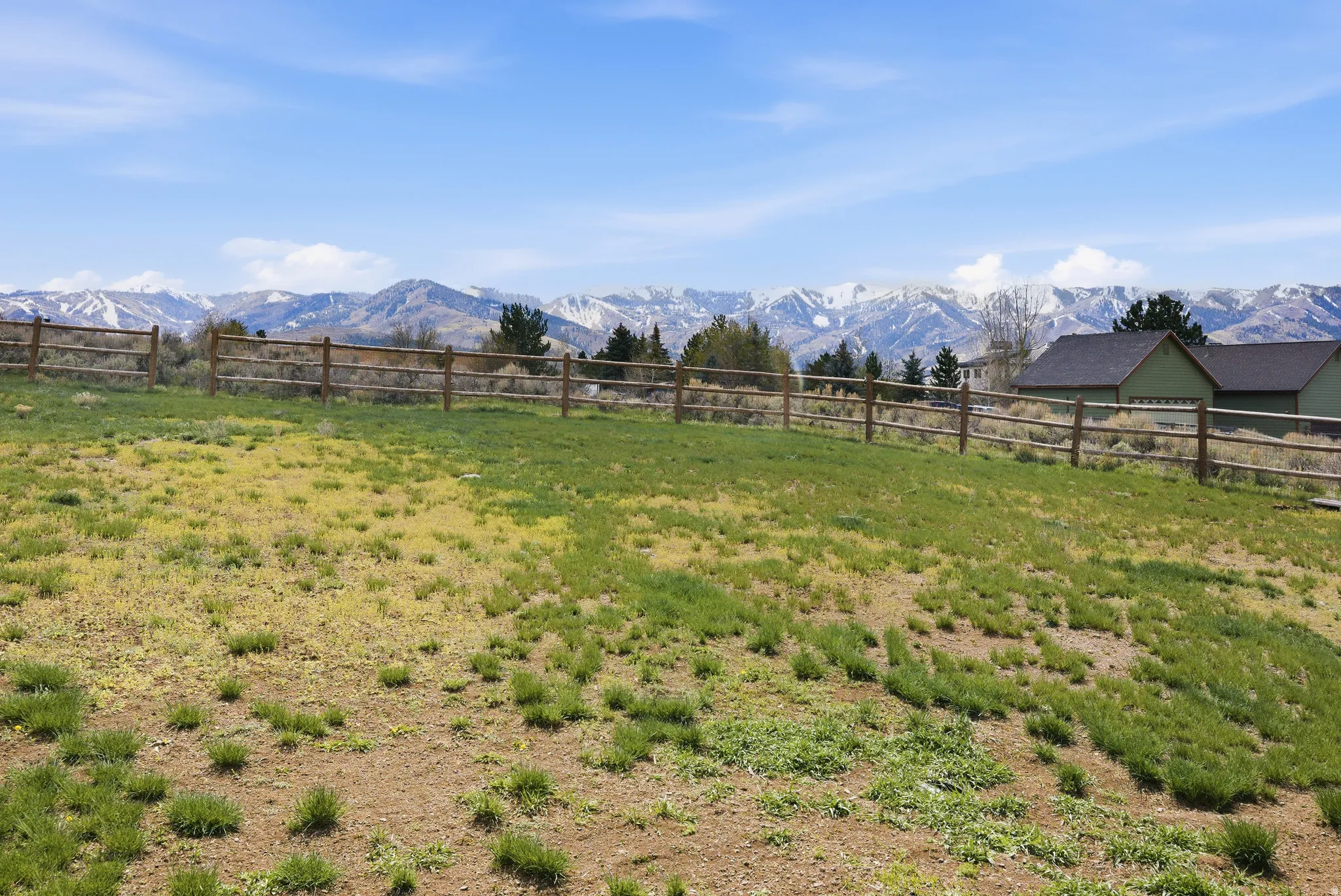 Expansive outdoor space featuring a wooden split-rail fence, a sloping grassy area, and a distant mountain range with snow-capped peaks