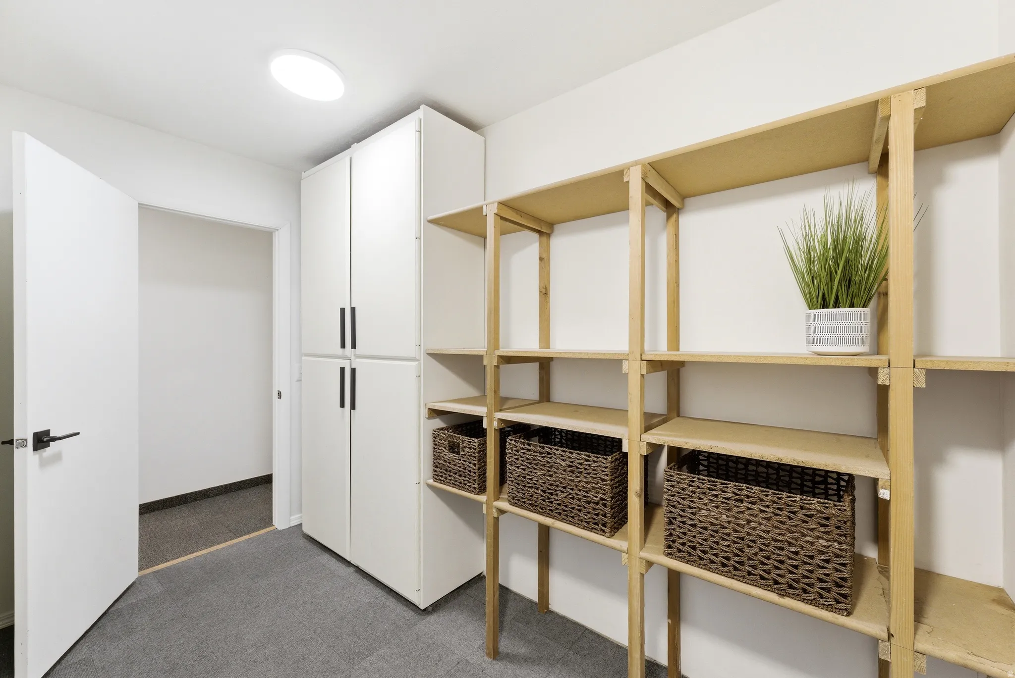 Dedicated storage area featuring expansive open shelving, built-in white cabinetry with matte black hardware, and an overhead flush-mount light fixture