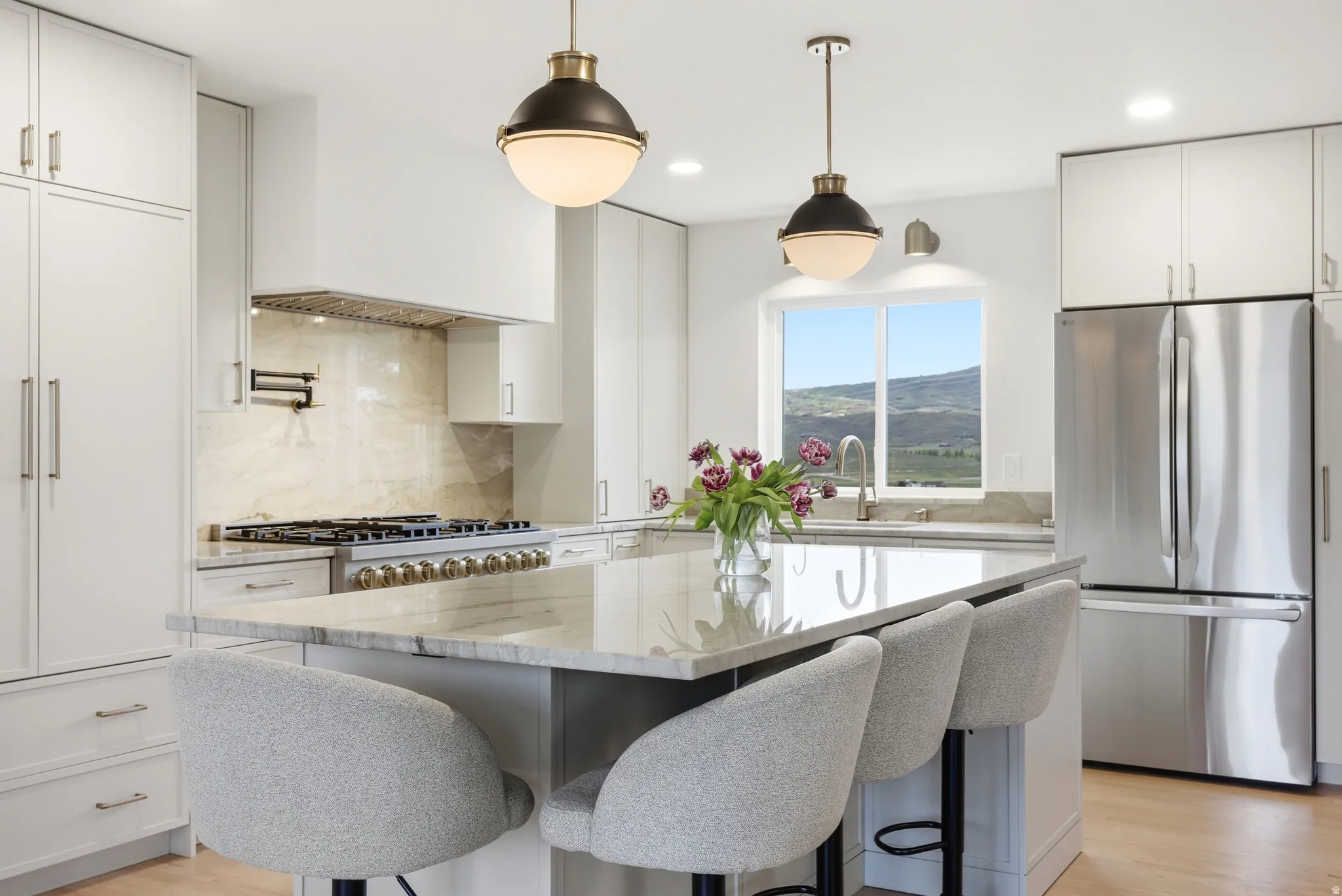 Gourmet kitchen featuring a large central island with seating, integrated stainless steel appliances, a professional range with pot filler, custom cabinetry, and natural stone countertops