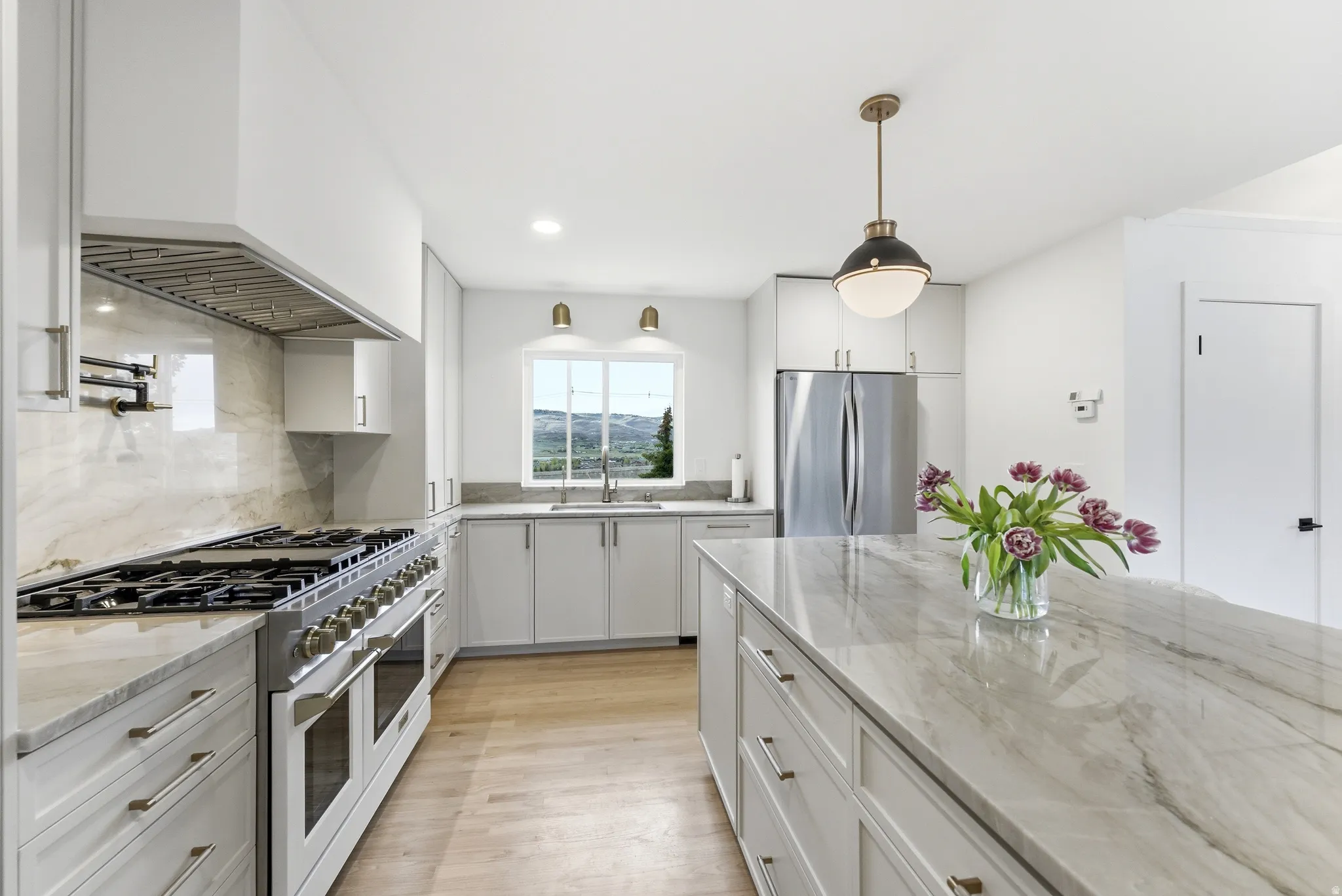 Gourmet kitchen featuring a substantial center island with stone countertops, a professional-grade range with a pot filler, extensive cabinet storage, stainless steel appliances, and wood-finish flooring