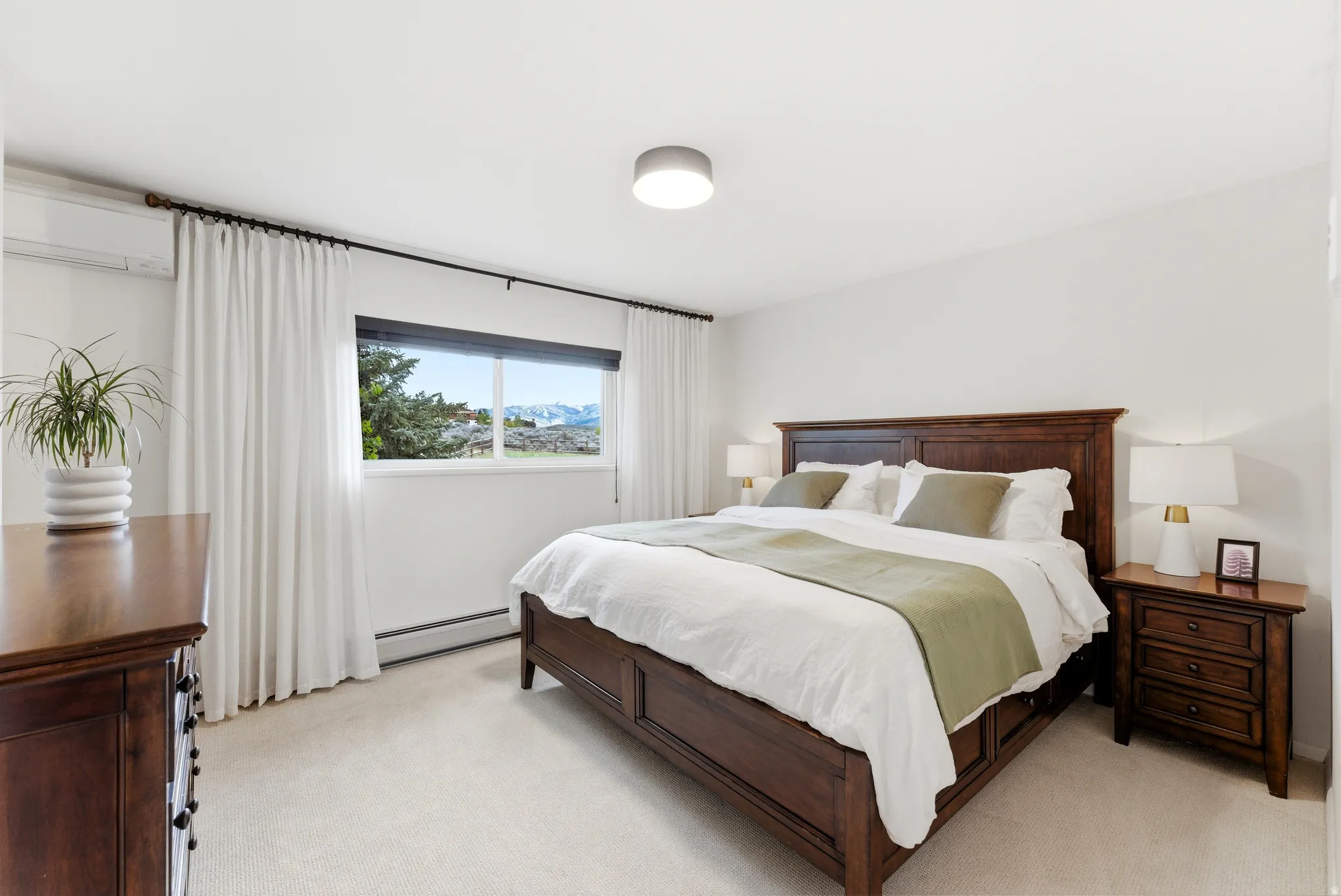 Bedroom featuring light-colored carpeting, a large window with white curtains, and a ceiling-mounted light fixture